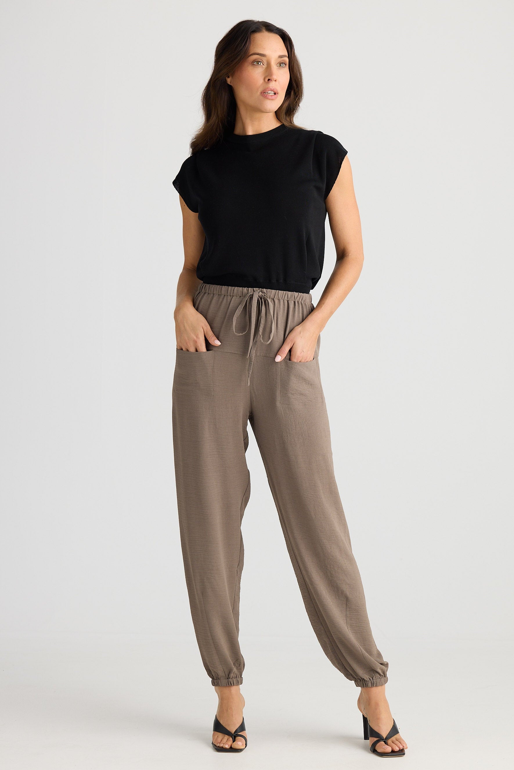 Woman wearing a black top and beige pants on a white background