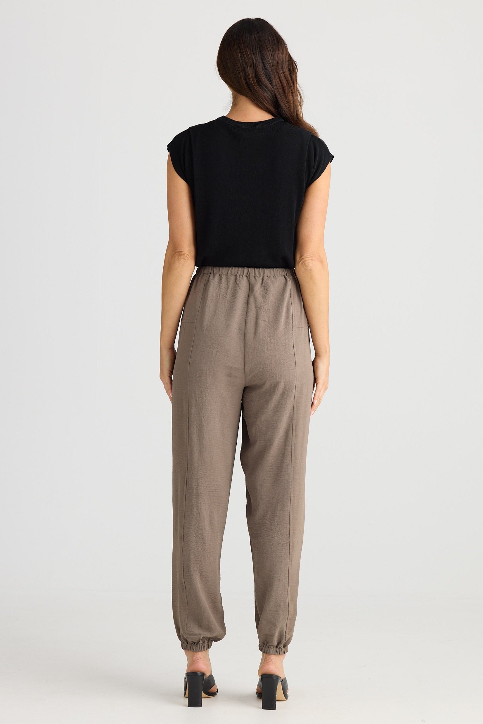 Woman wearing a black top and beige pants on a white background