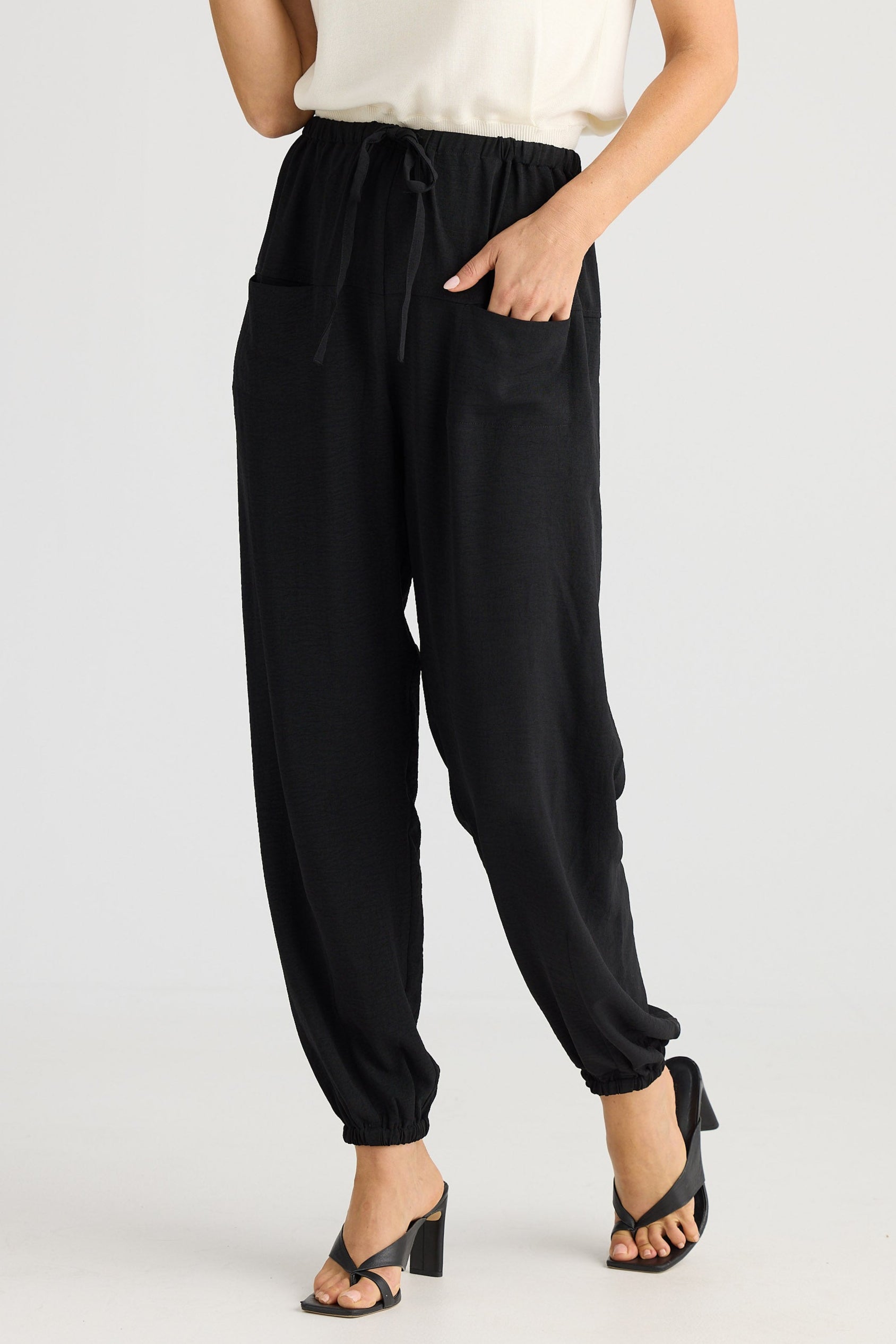 Person wearing black jogger pants and a white top on a light gray background