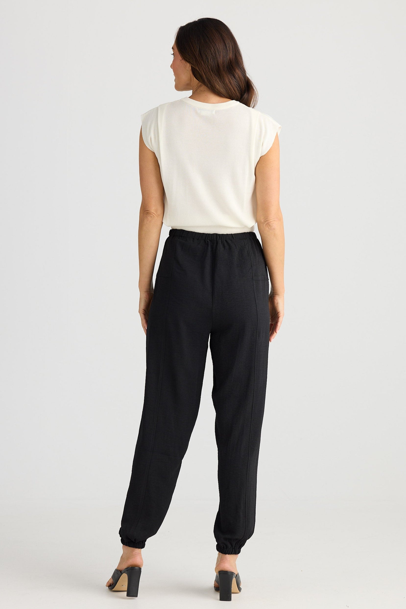 Woman wearing a white top and black pants on a light gray background