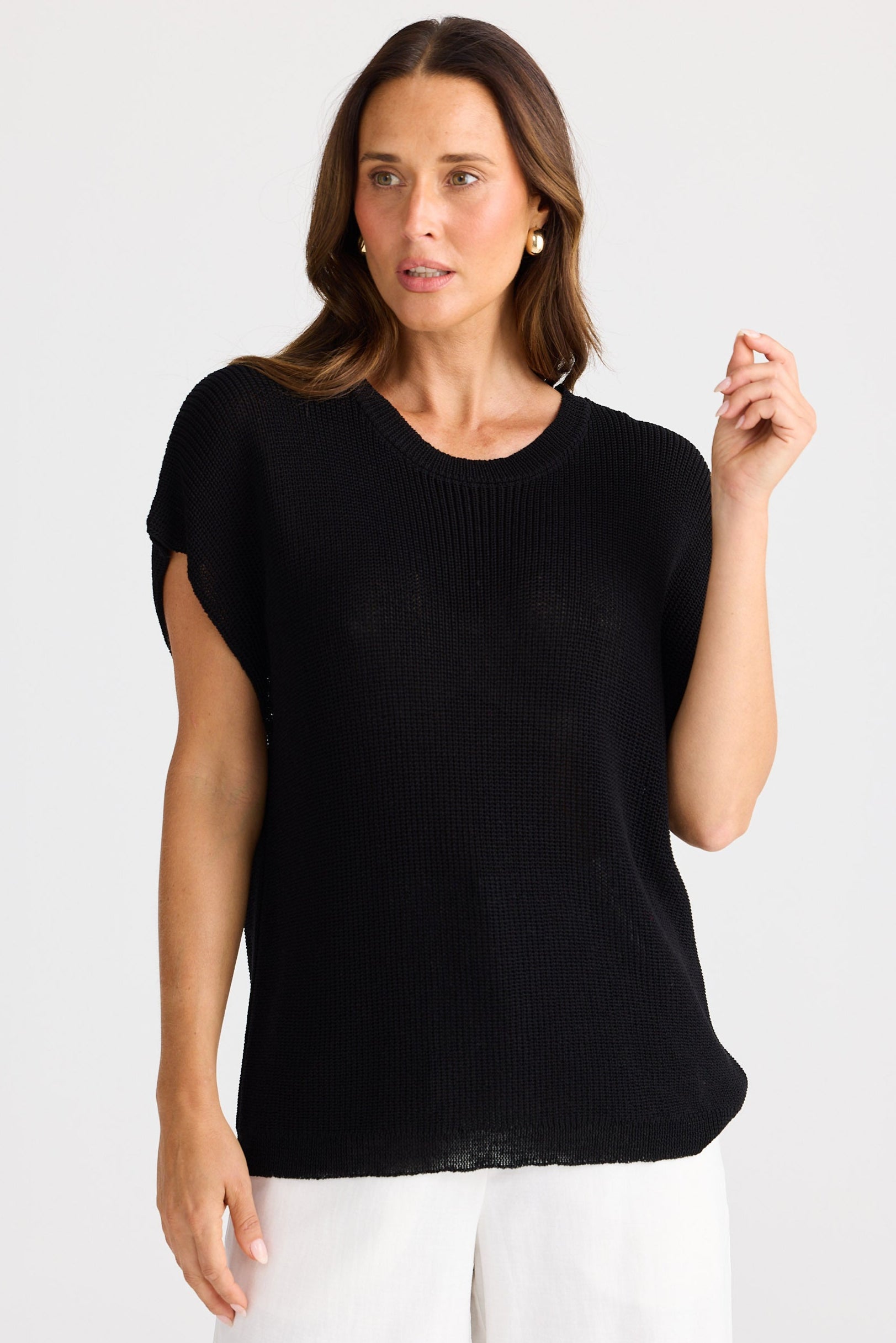 Woman wearing a black top and white pants against a white background