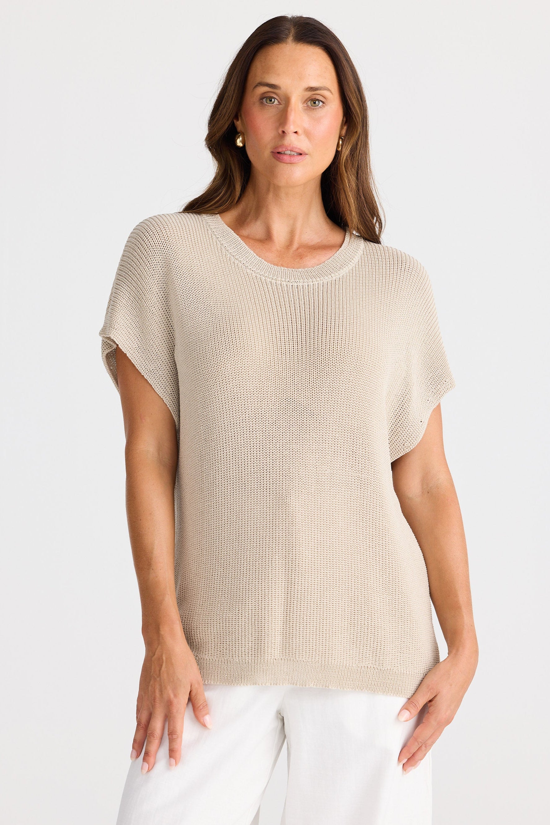 Woman wearing a beige knit top and white pants on a white background