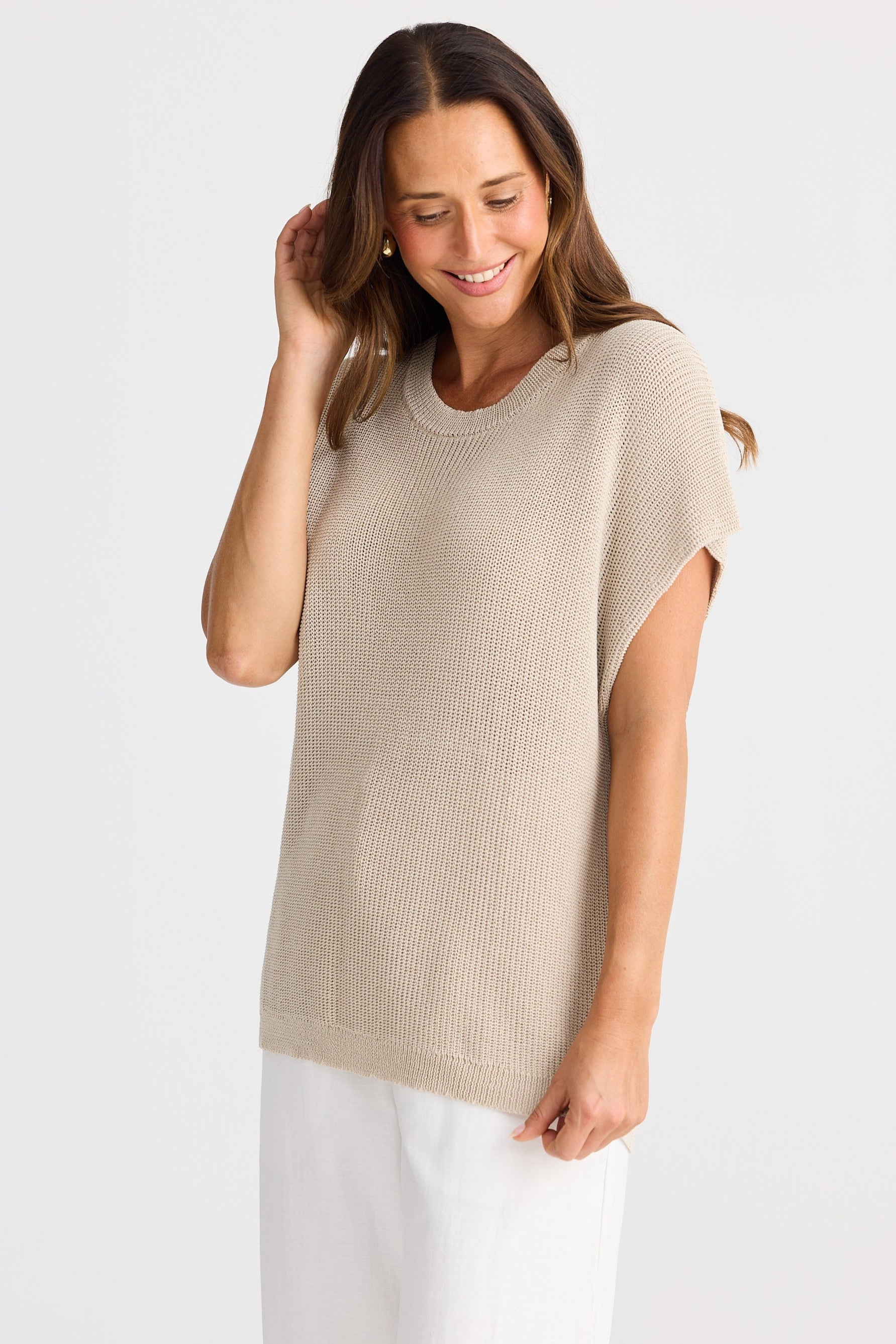 Woman wearing a beige sleeveless top and white pants on a light background