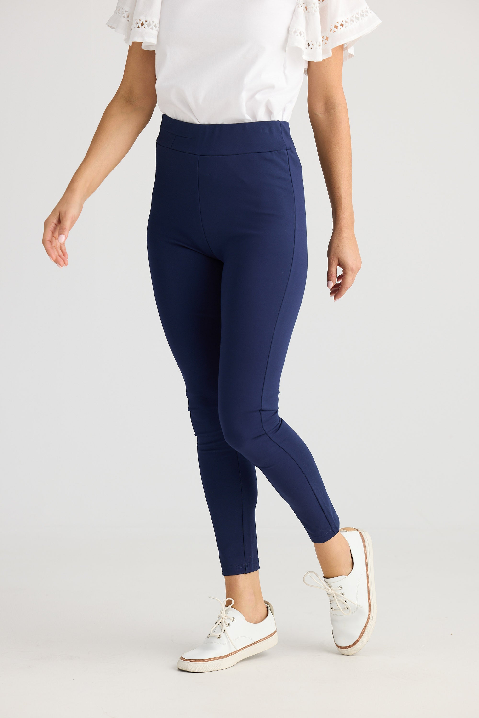 Person wearing navy leggings with a white top and sneakers on a light gray background