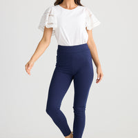 Woman wearing a white top and blue leggings on a light gray background