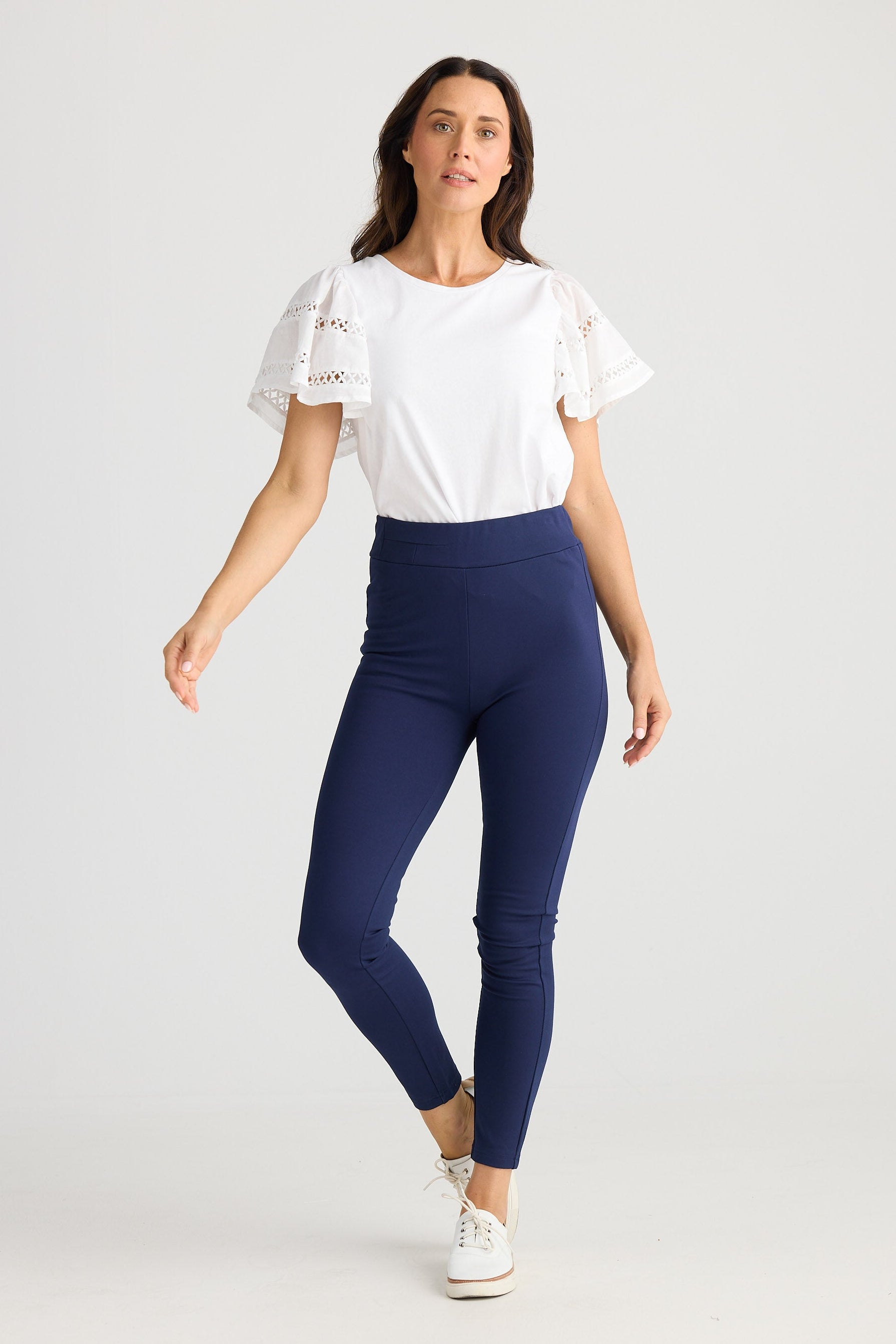 Woman wearing a white top and blue leggings on a light gray background