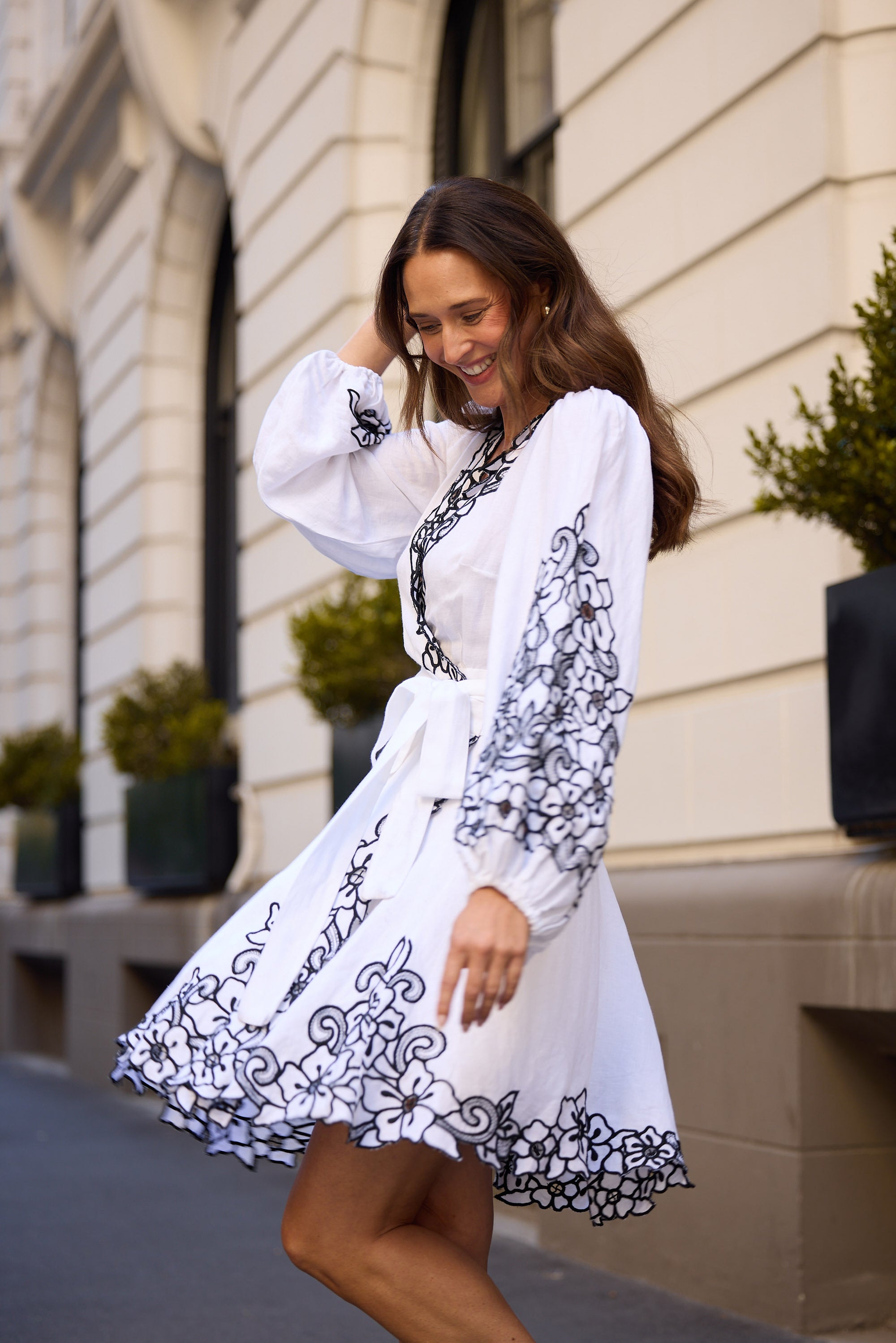 Woman in a white dress with black embroidery walking outdoors.