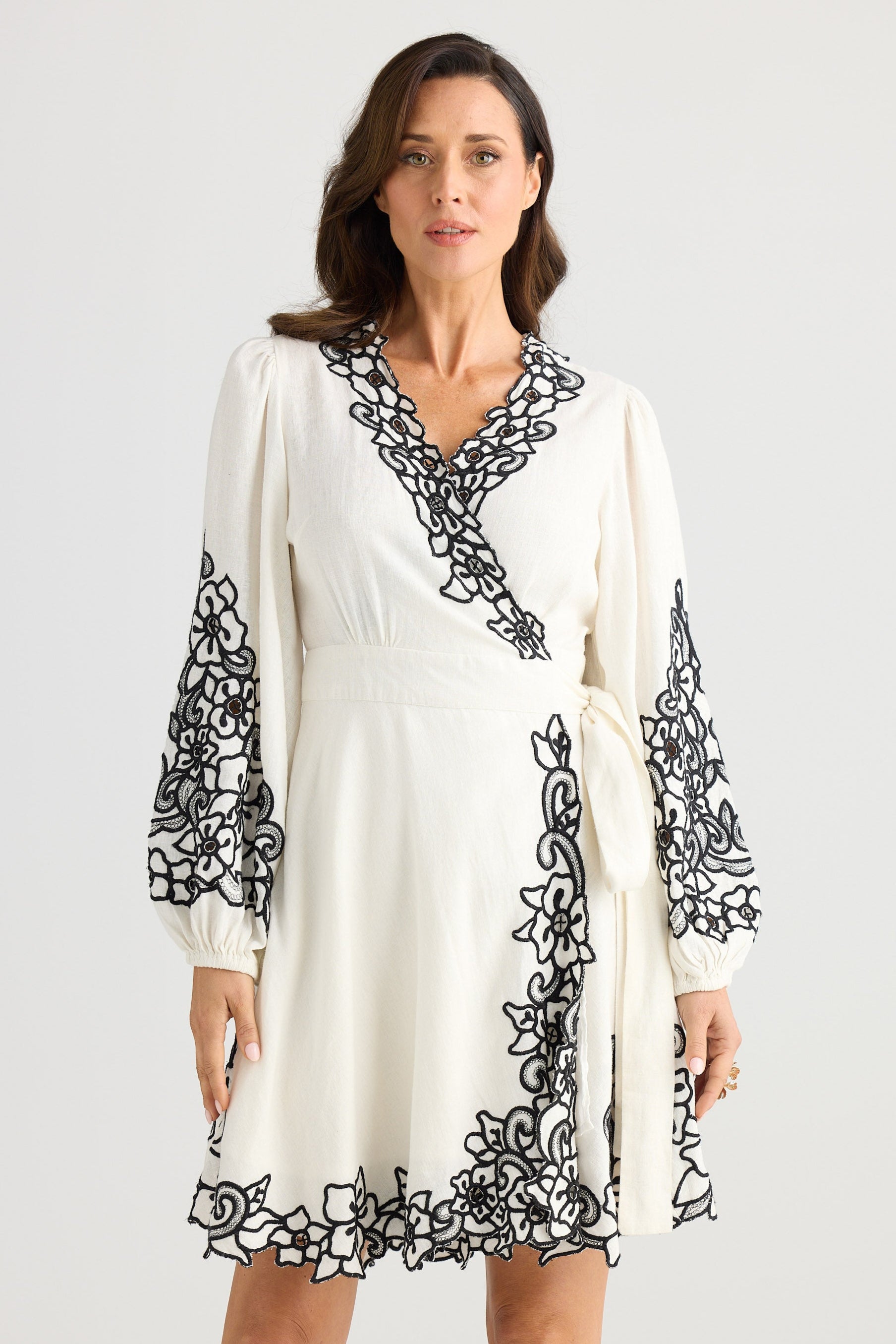 Woman wearing a white dress with black floral embroidery on a plain background