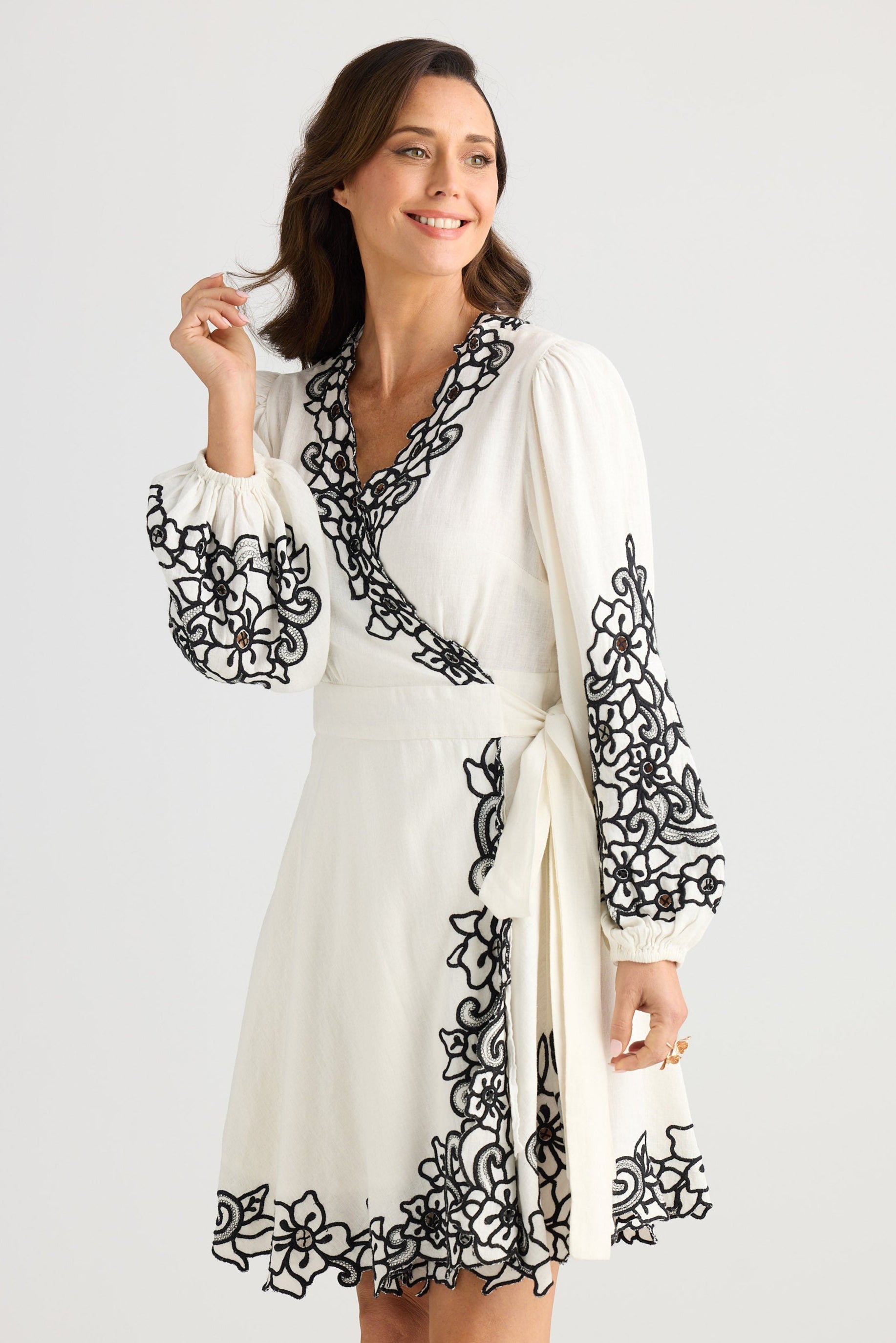 Woman wearing a white dress with black floral embroidery on a white background