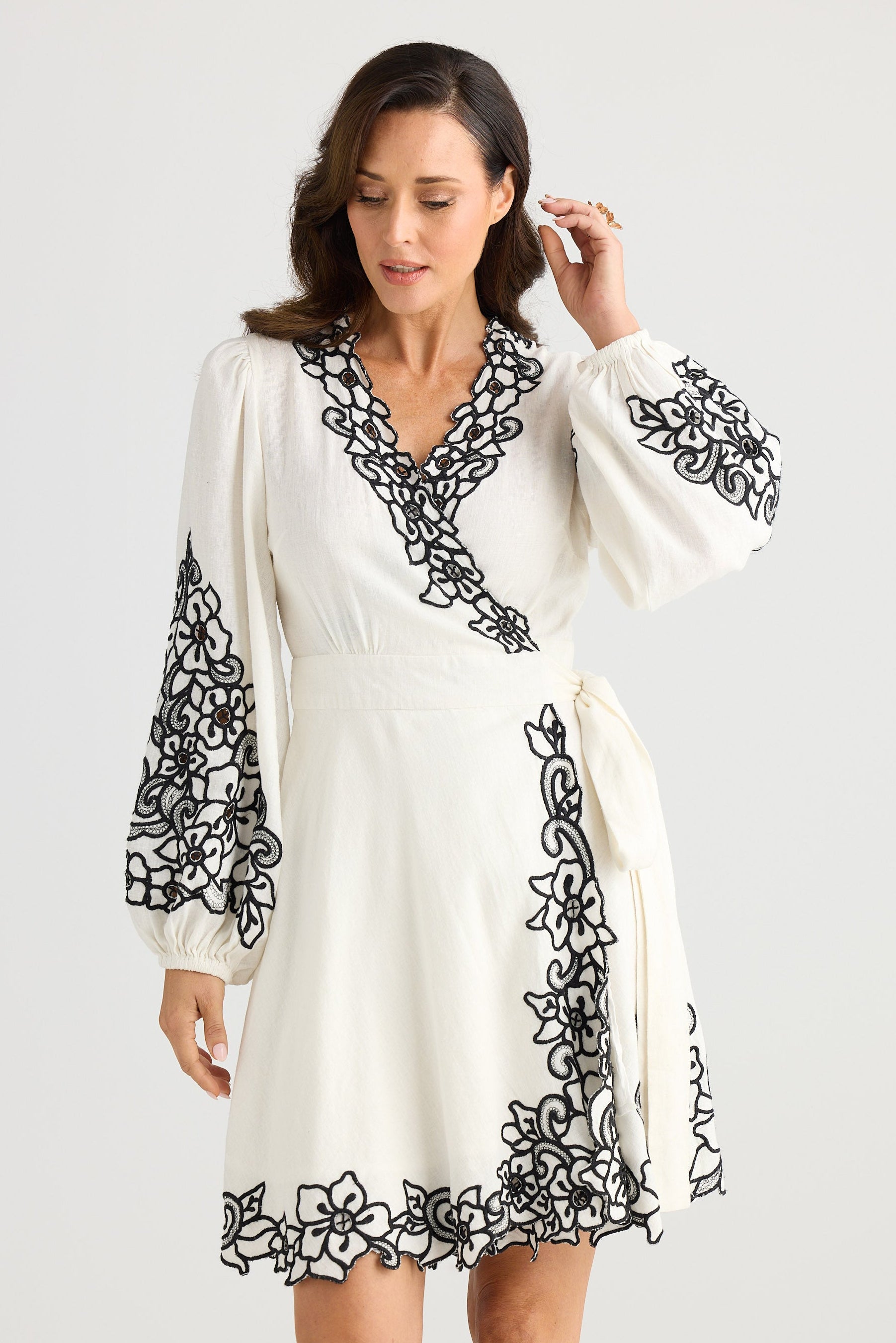 Woman wearing a white dress with black floral embroidery on a white background
