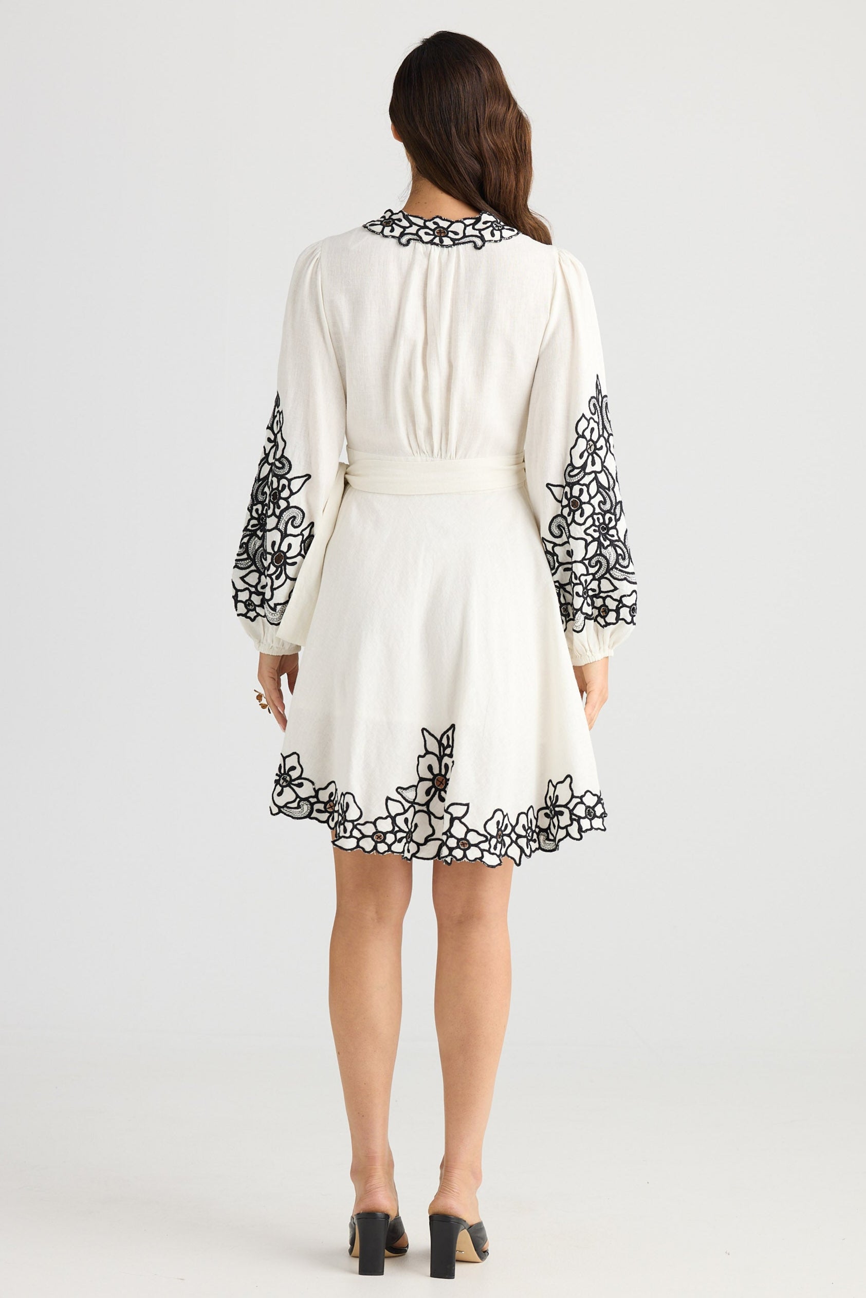 White dress with black floral embroidery on sleeves and hem, worn by a model against a white background