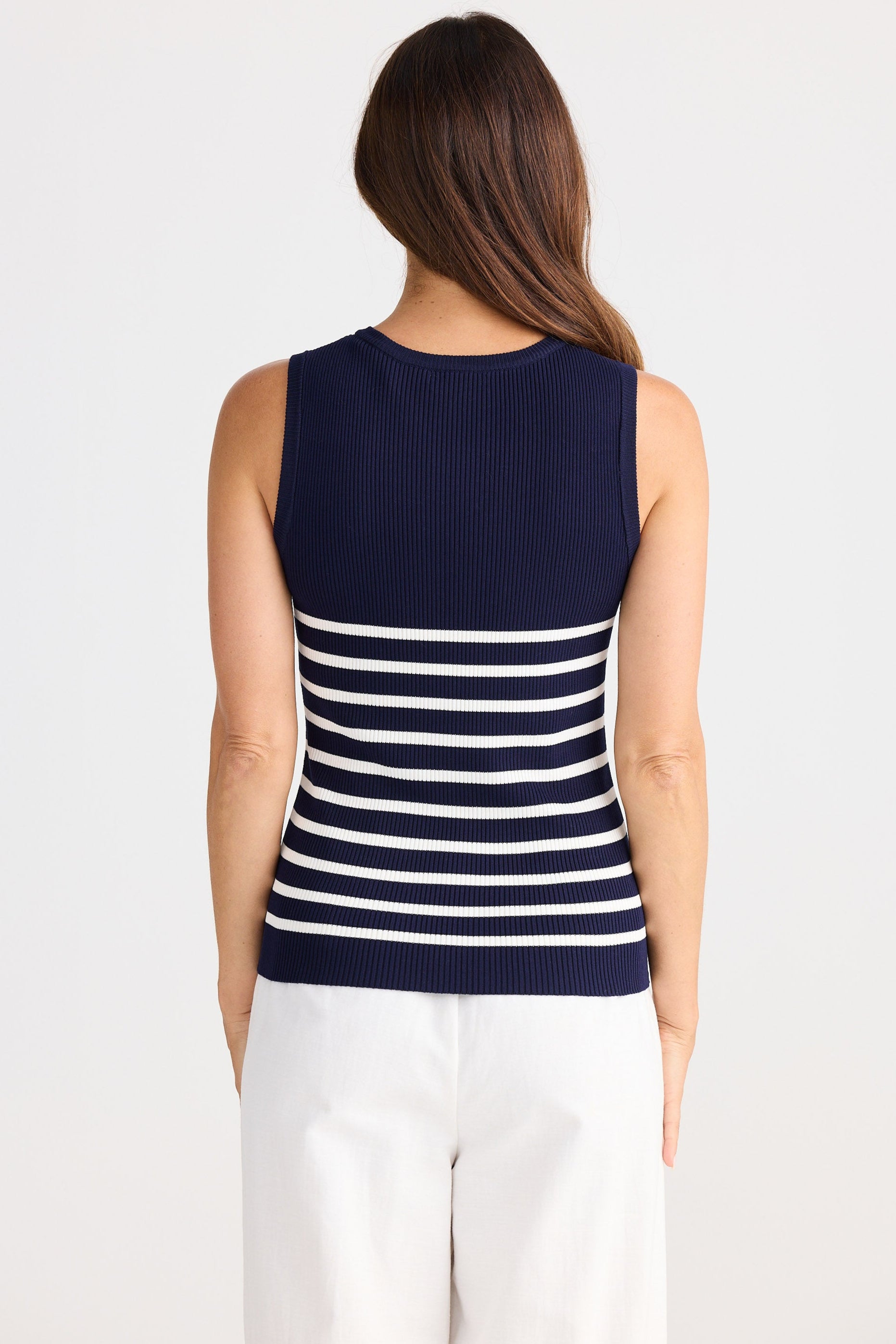 Woman wearing a navy blue sleeveless top with white stripes on a plain background