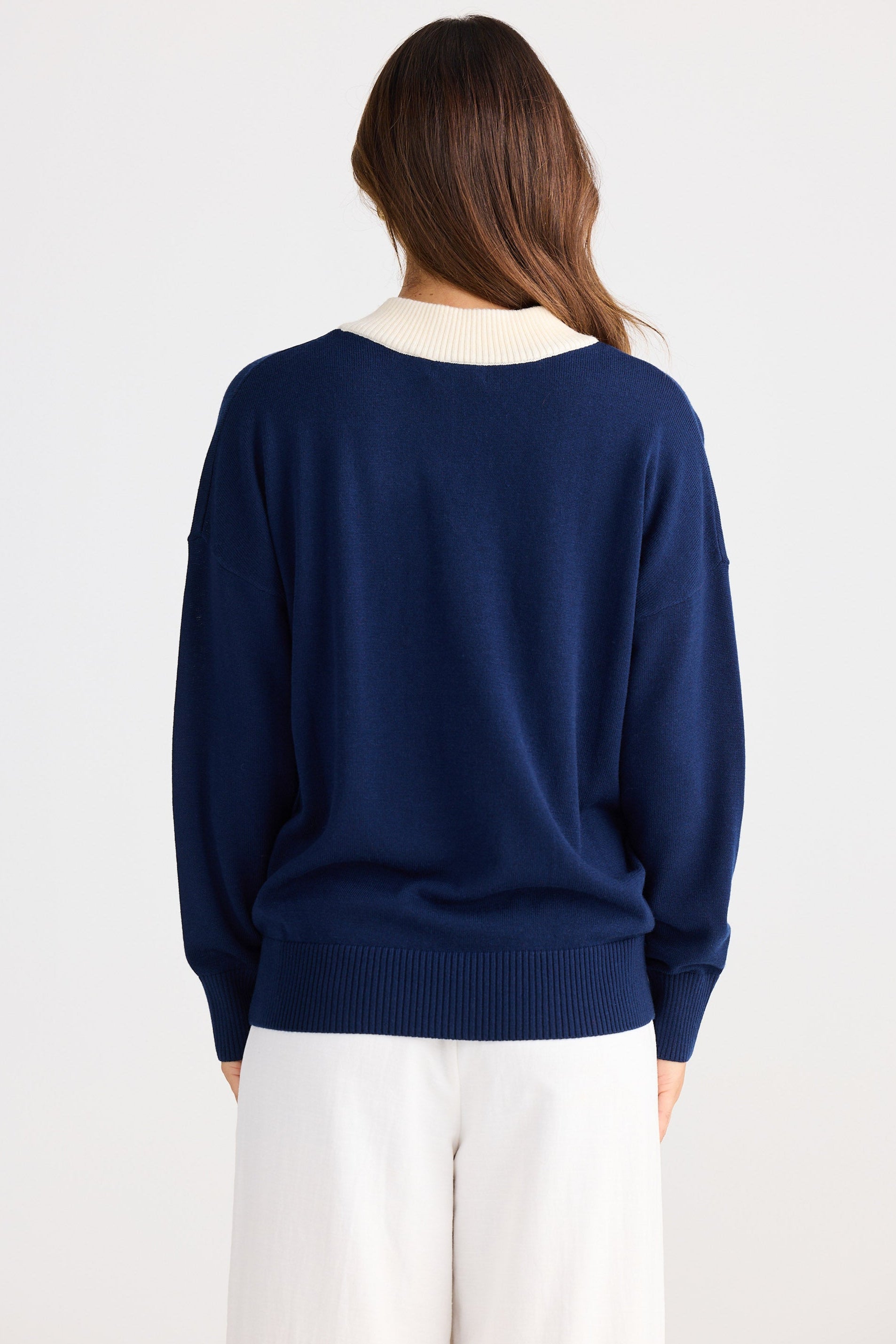 Person wearing a navy sweater and white pants on a plain background