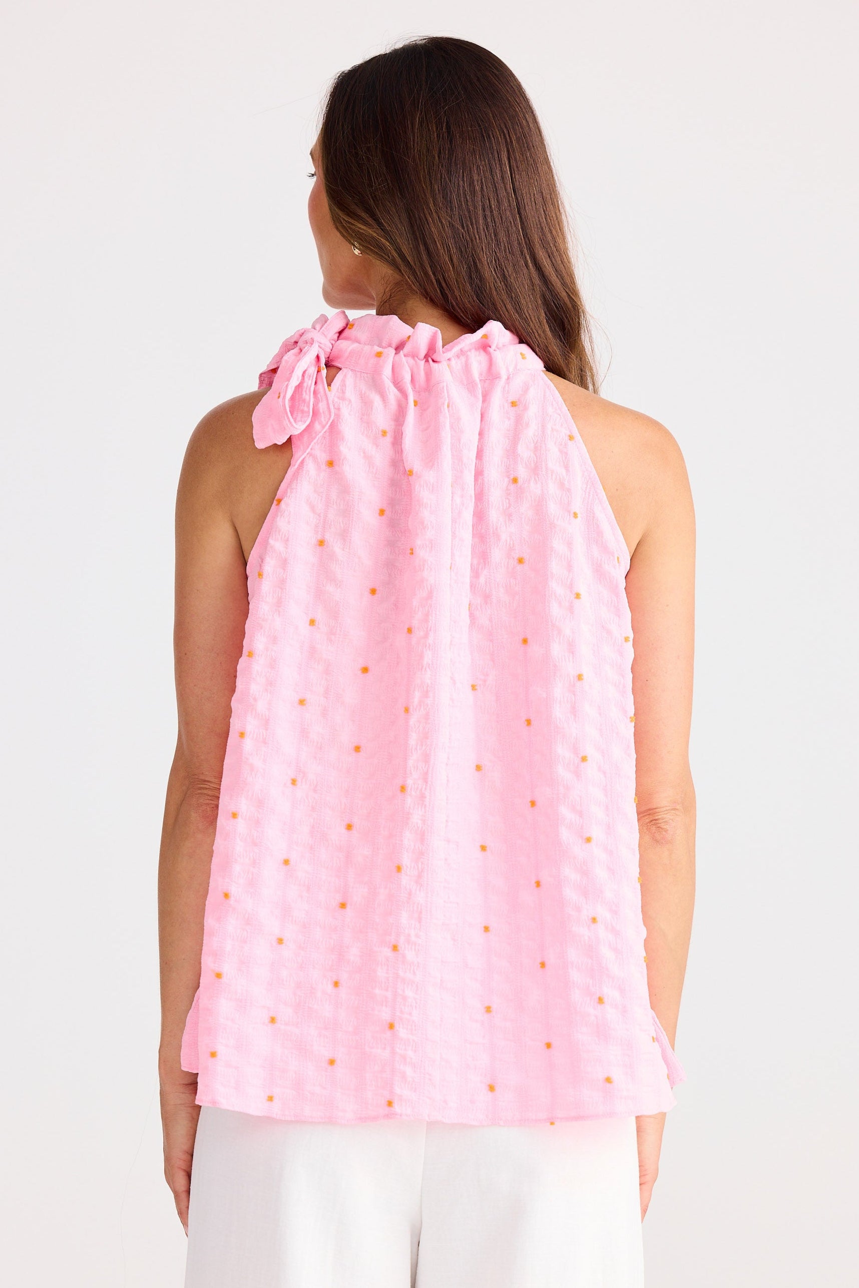 Woman wearing a pink sleeveless top with a halter neck design on a white background