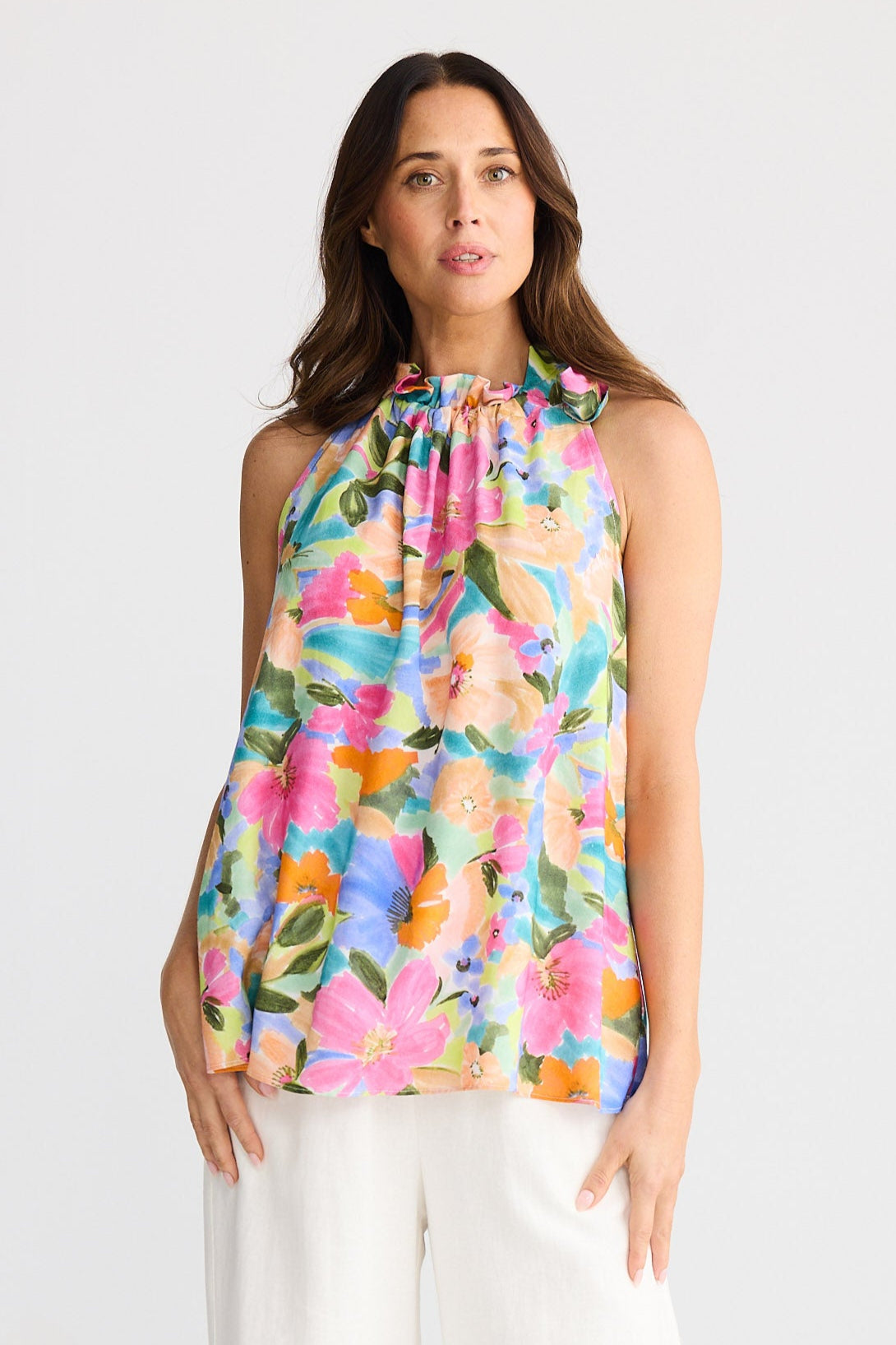 Woman wearing a colorful floral top and white pants on a white background