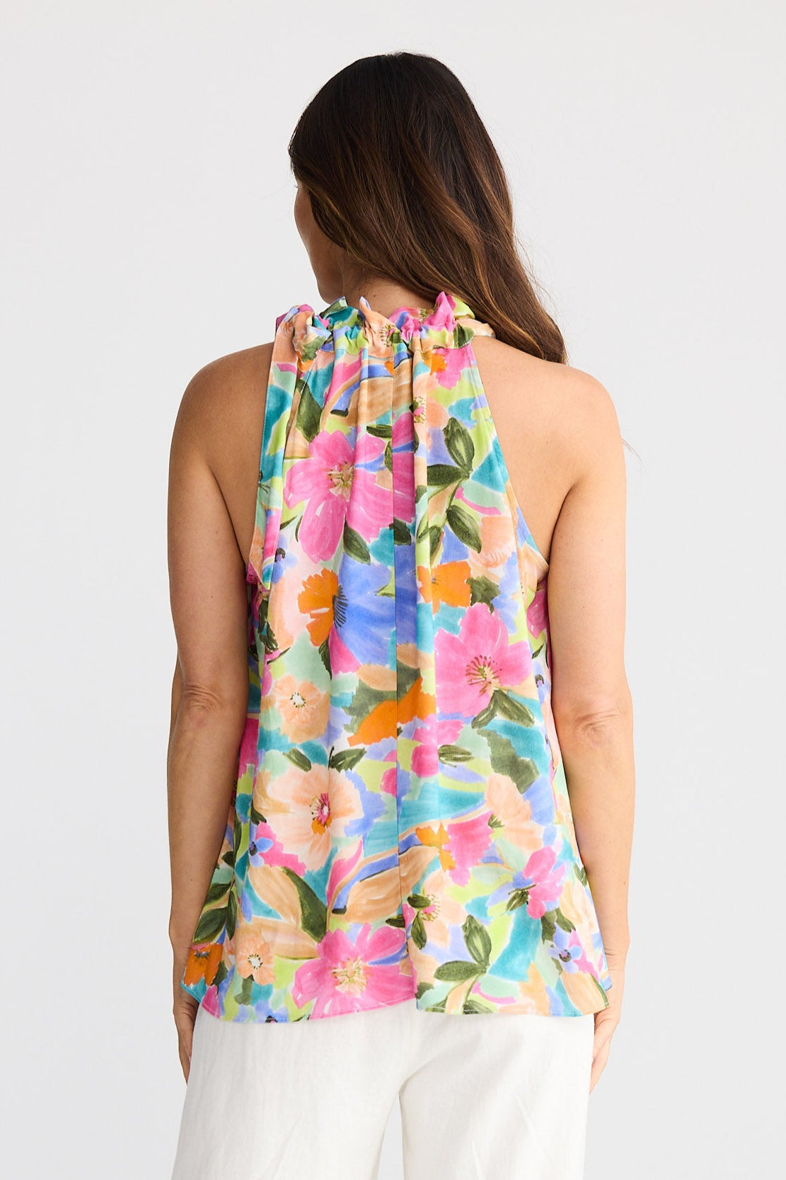 Woman wearing a colorful floral sleeveless top and white pants on a white background
