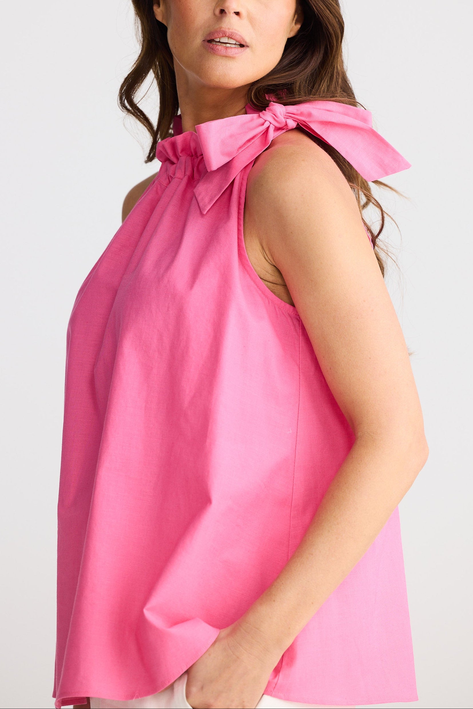 Woman wearing a pink sleeveless top with a bow detail on a white background