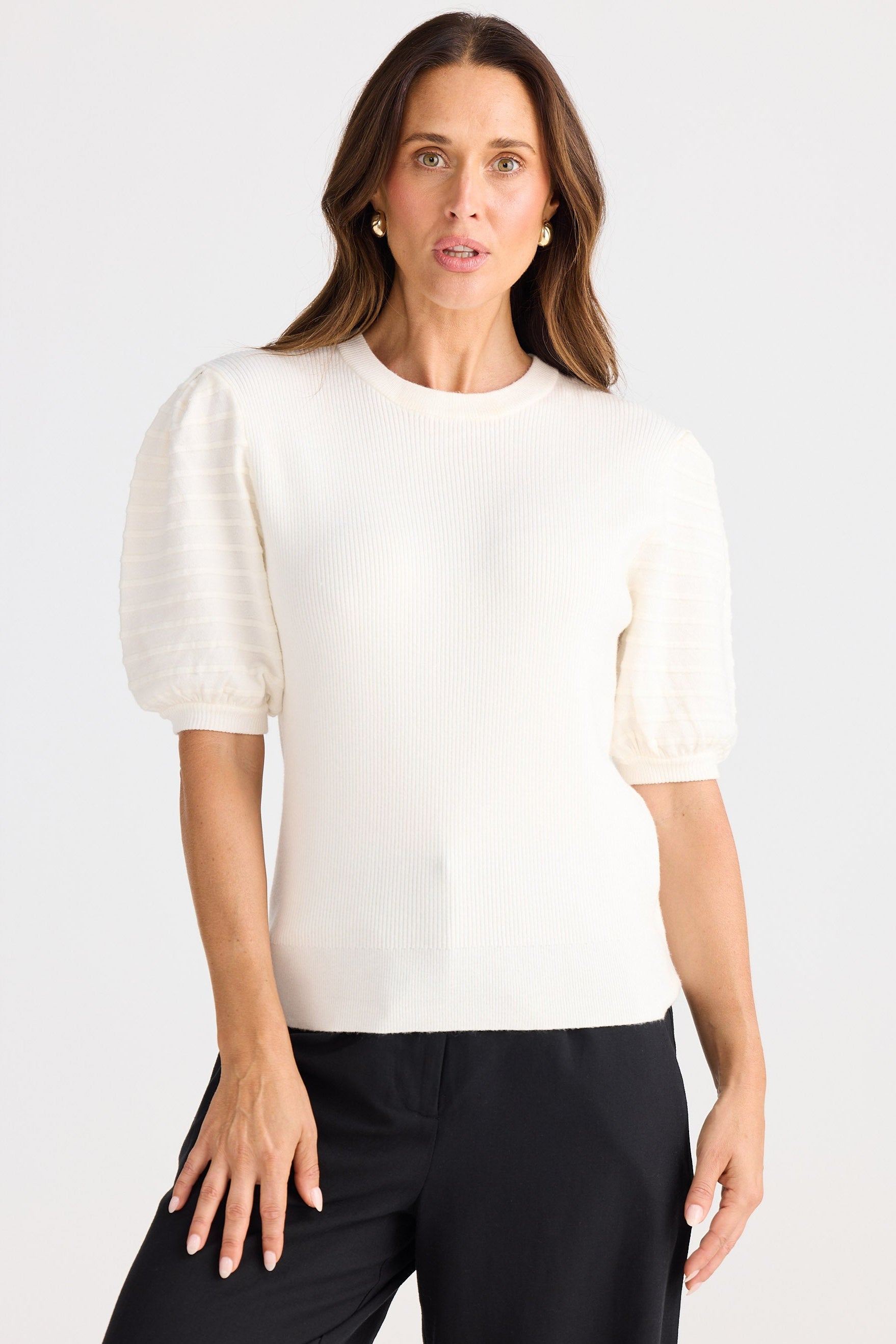 Woman wearing a white knit top with puff sleeves and black pants on a white background