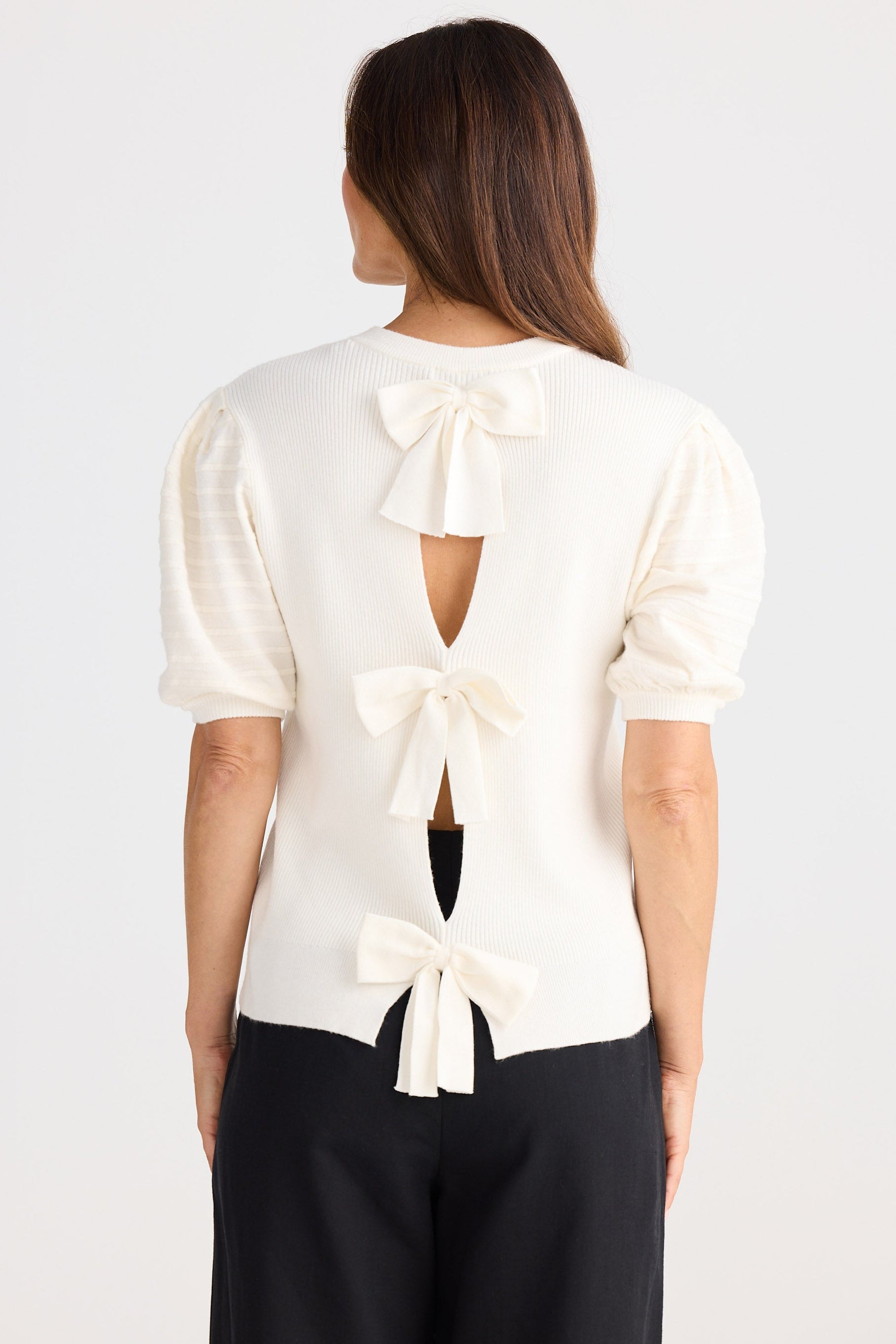 Woman wearing a white blouse with bow details on a plain background