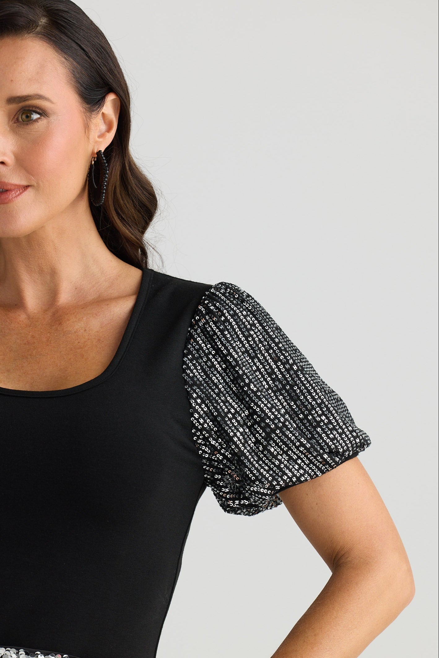 Woman wearing a black top with silver sequin sleeves and silver pants against a plain background