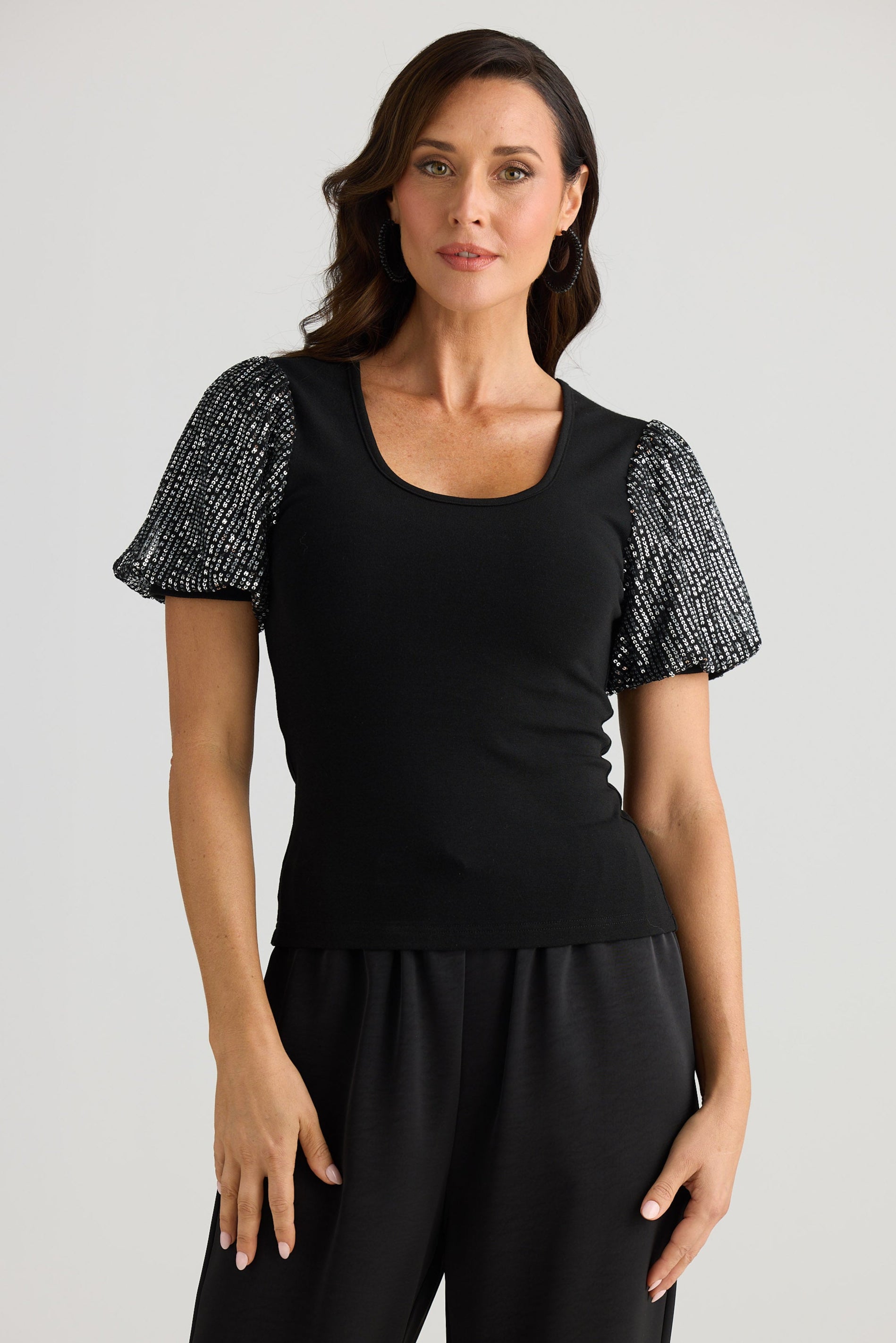 Woman wearing a black outfit with a textured black and white top on a gray background