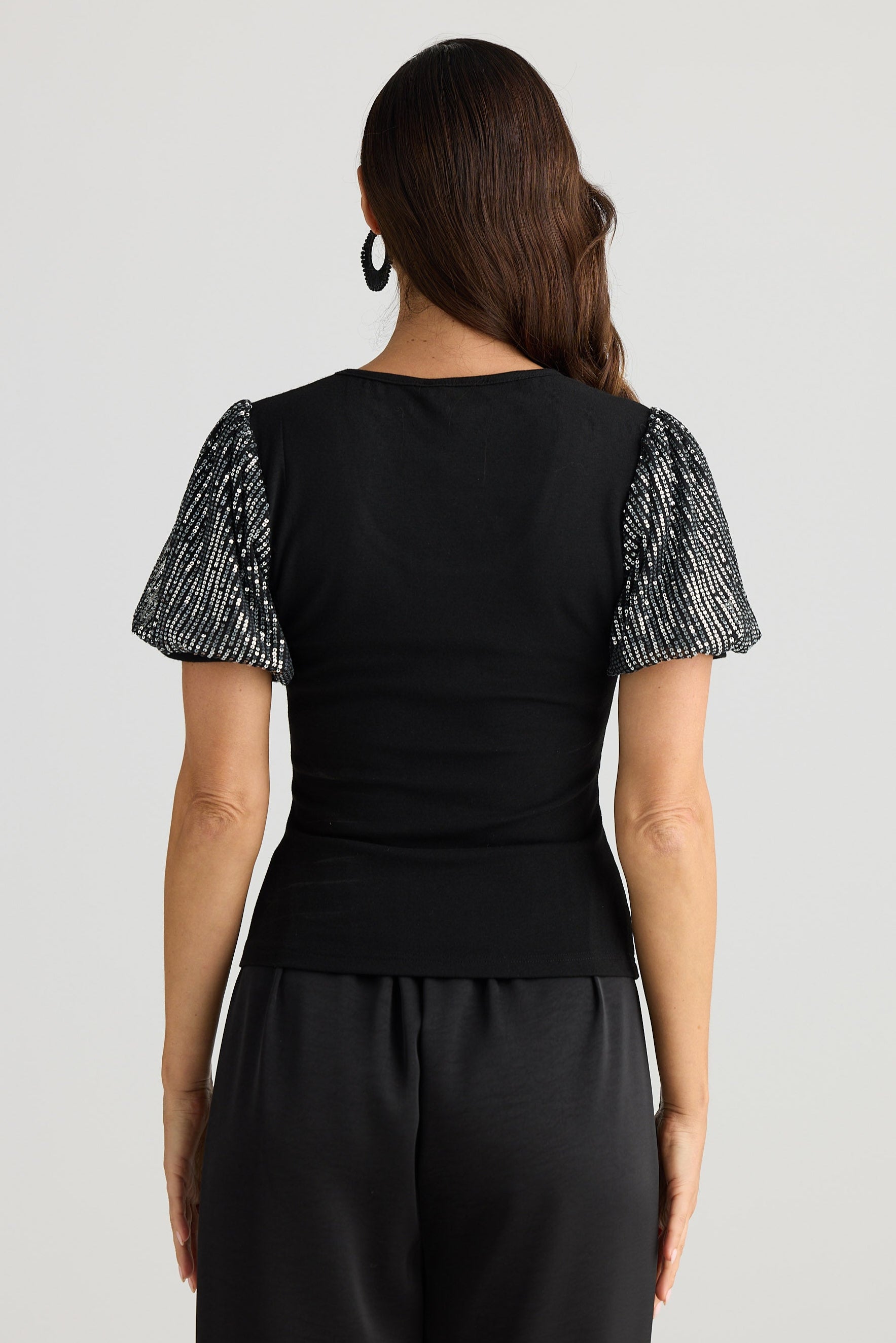 Woman wearing a black outfit with sequin sleeves on a white background