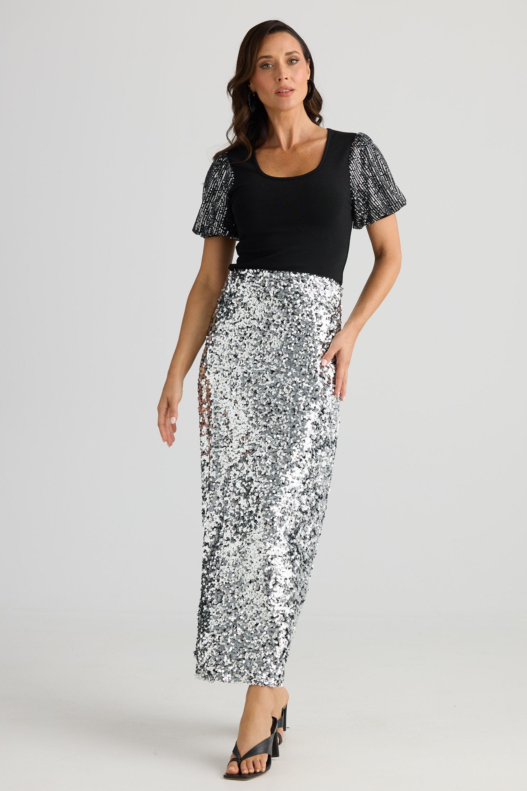 Woman wearing a black top with lace sleeves and a white floral skirt on a white background
