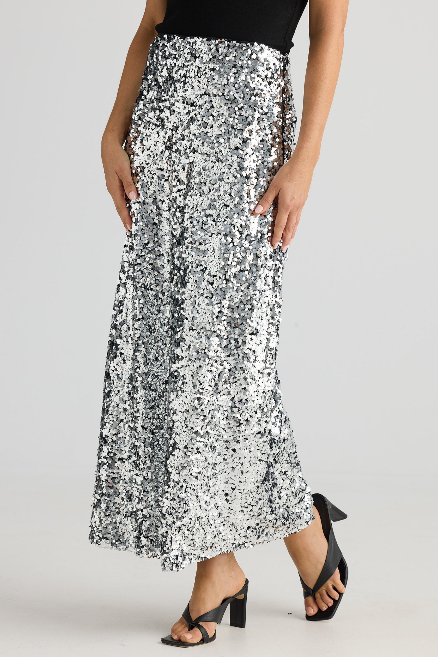 Person wearing a black top and silver sequin skirt on a white background