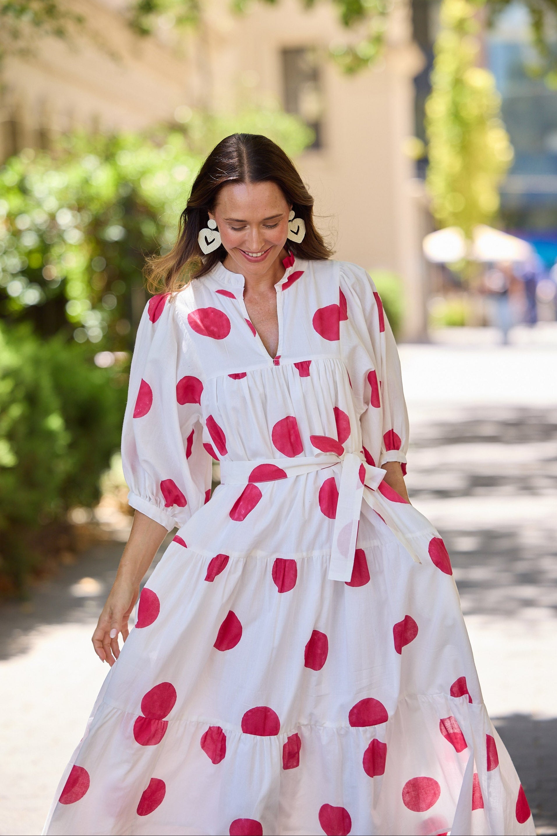 Woman wearing a white dress with red polka dots walking outdoors.