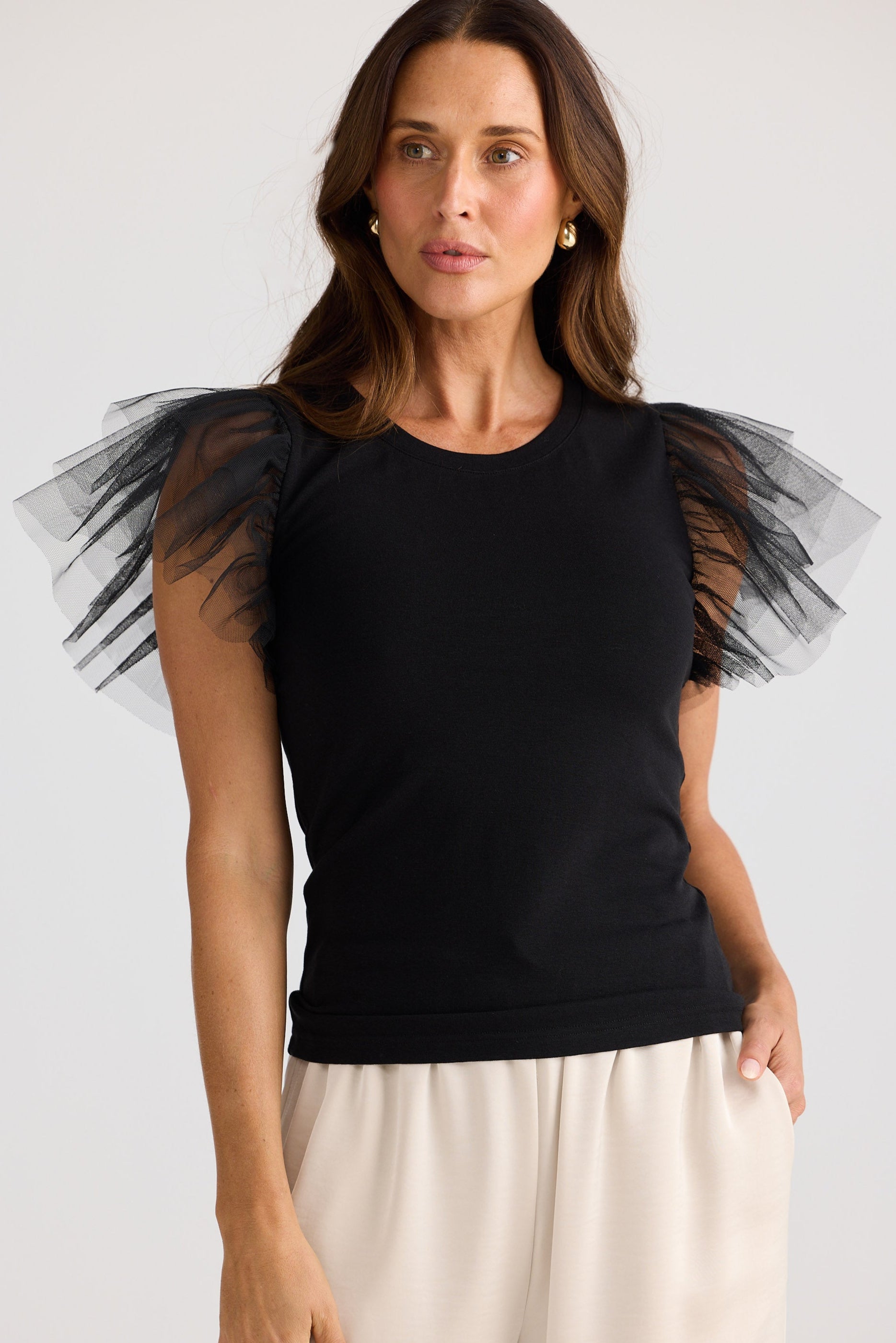 Woman wearing a black top with sheer tulle sleeves against a white background