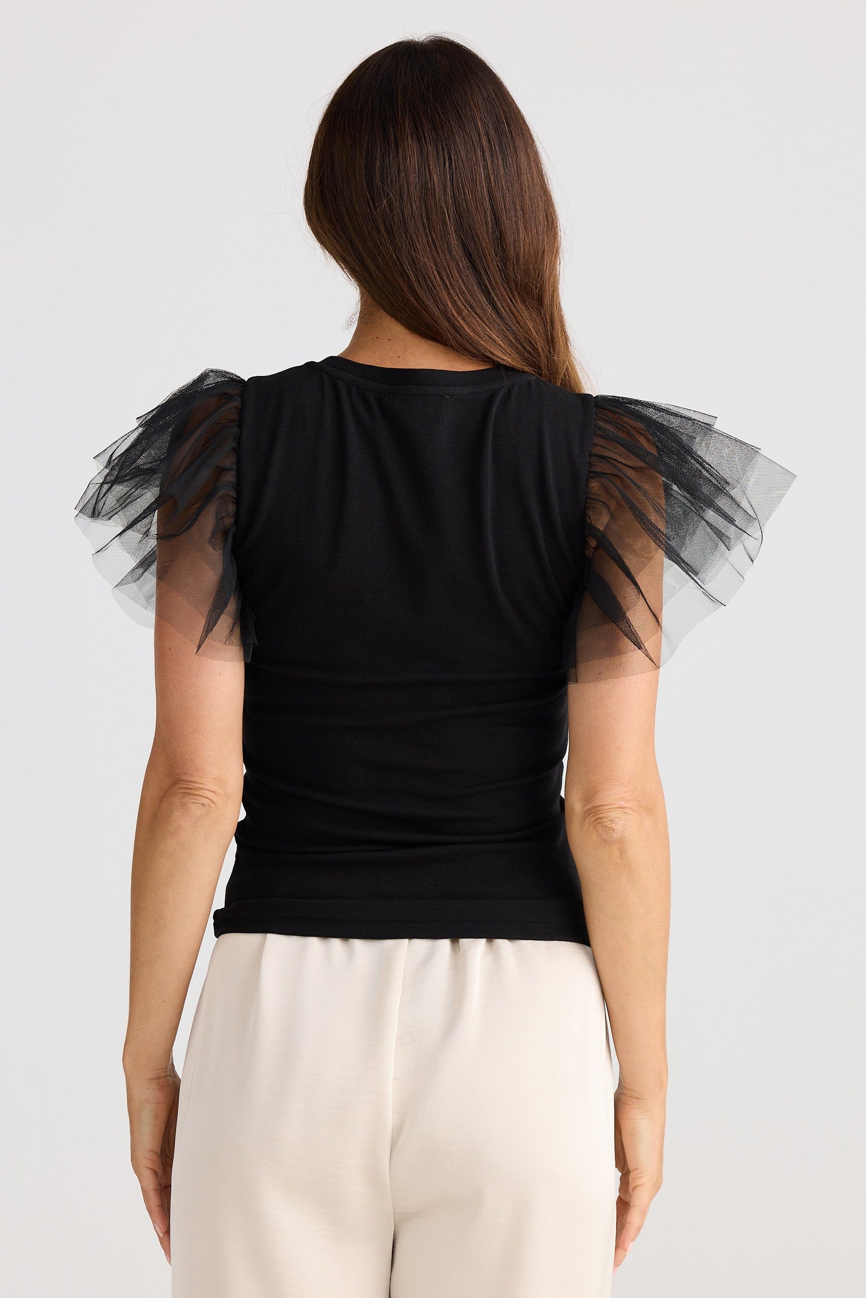 Black top with sheer sleeves worn by a person on a white background