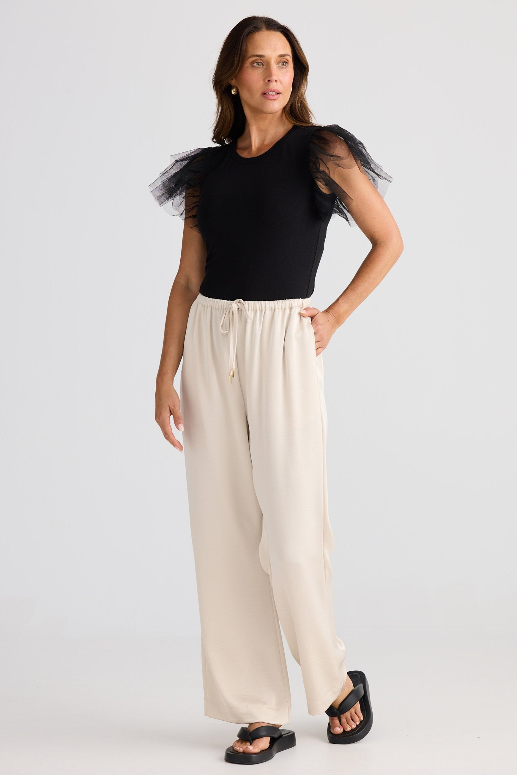 Woman wearing a black top with sheer sleeves and beige wide-leg pants on a white background