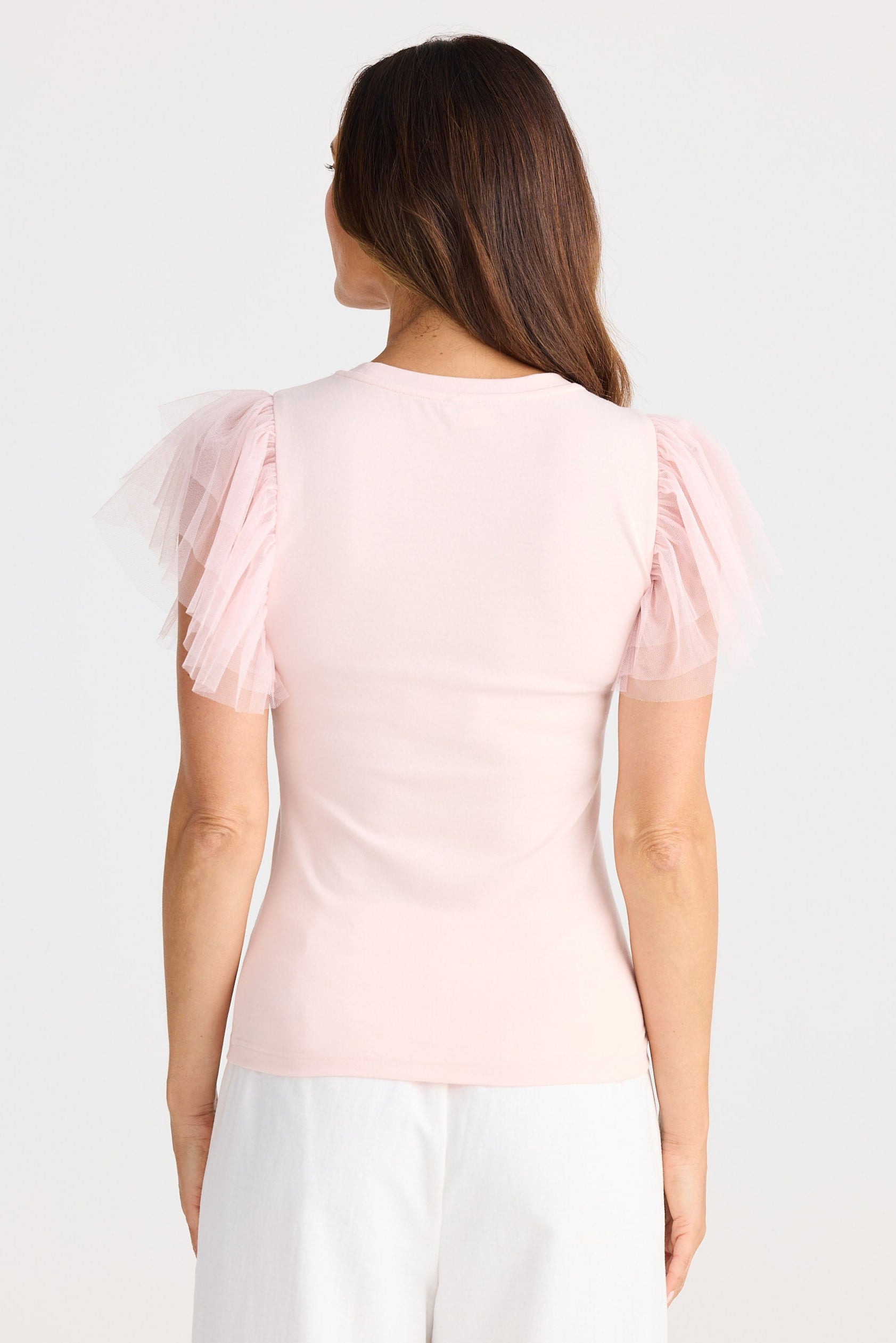 Woman wearing a light pink top with sheer sleeves on a white background