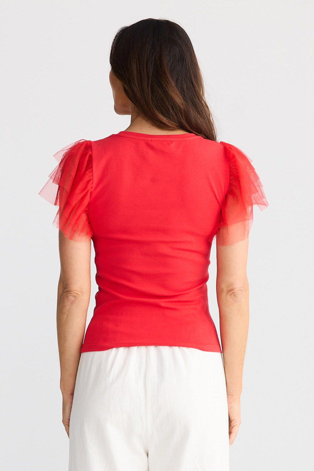 Woman wearing a red top and white pants on a white background