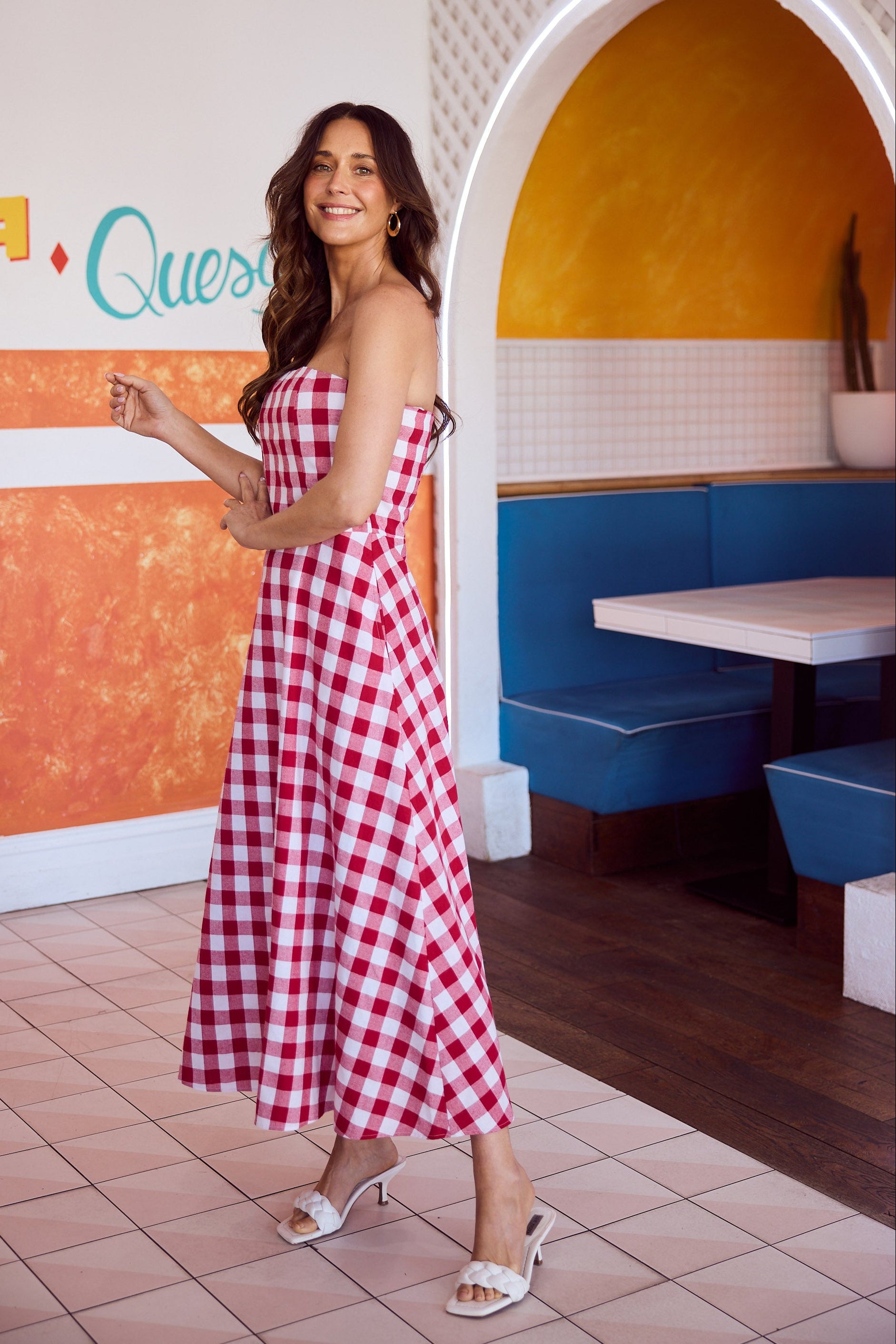 Woman in a red and white checkered dress standing in a colorful diner.