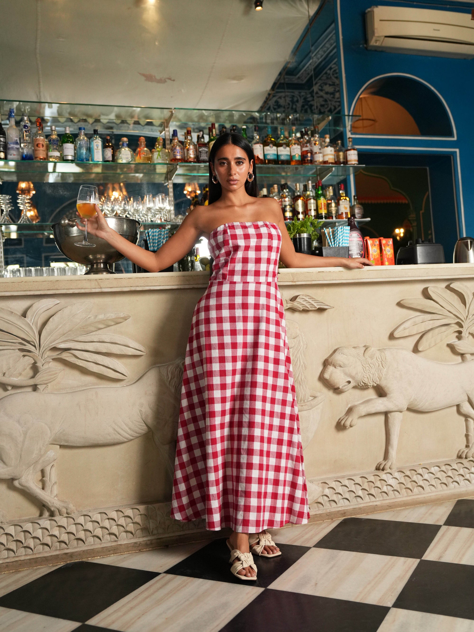 Woman in a red and white checkered dress standing behind a bar counter.