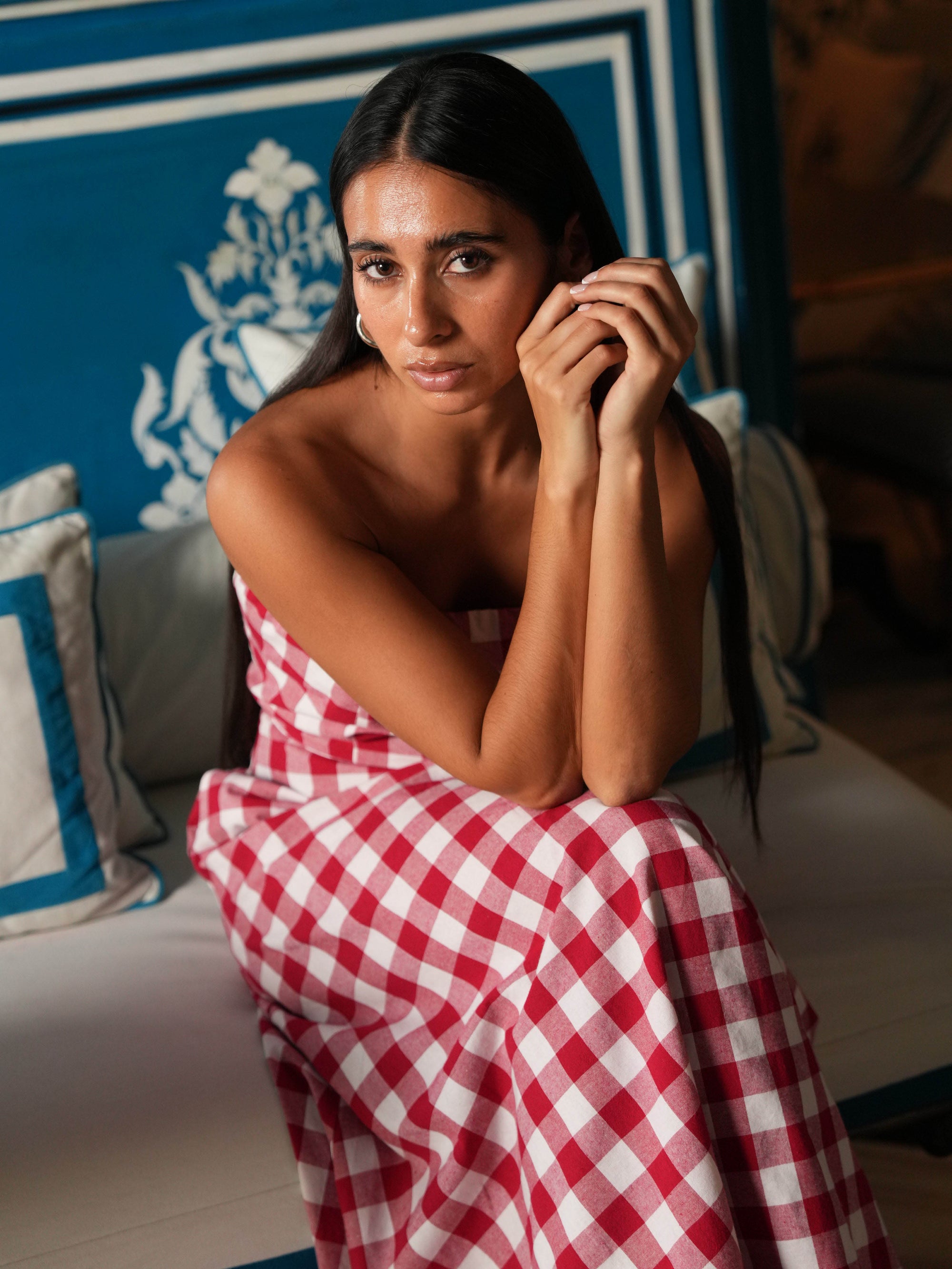 Woman in a red and white checkered dress in a room with blue walls and decorative pillows.