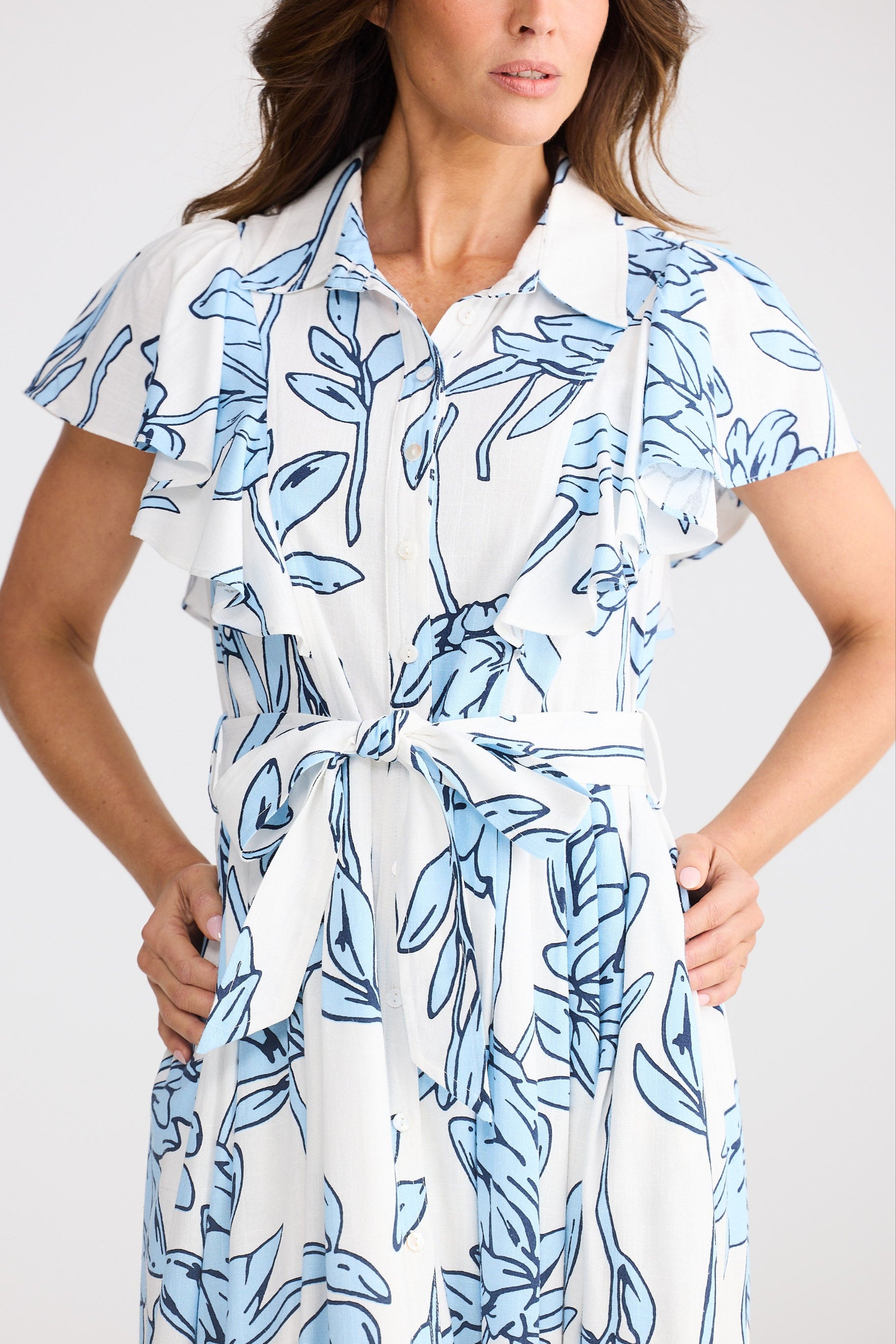 Woman wearing a white dress with blue leaf pattern against a plain background