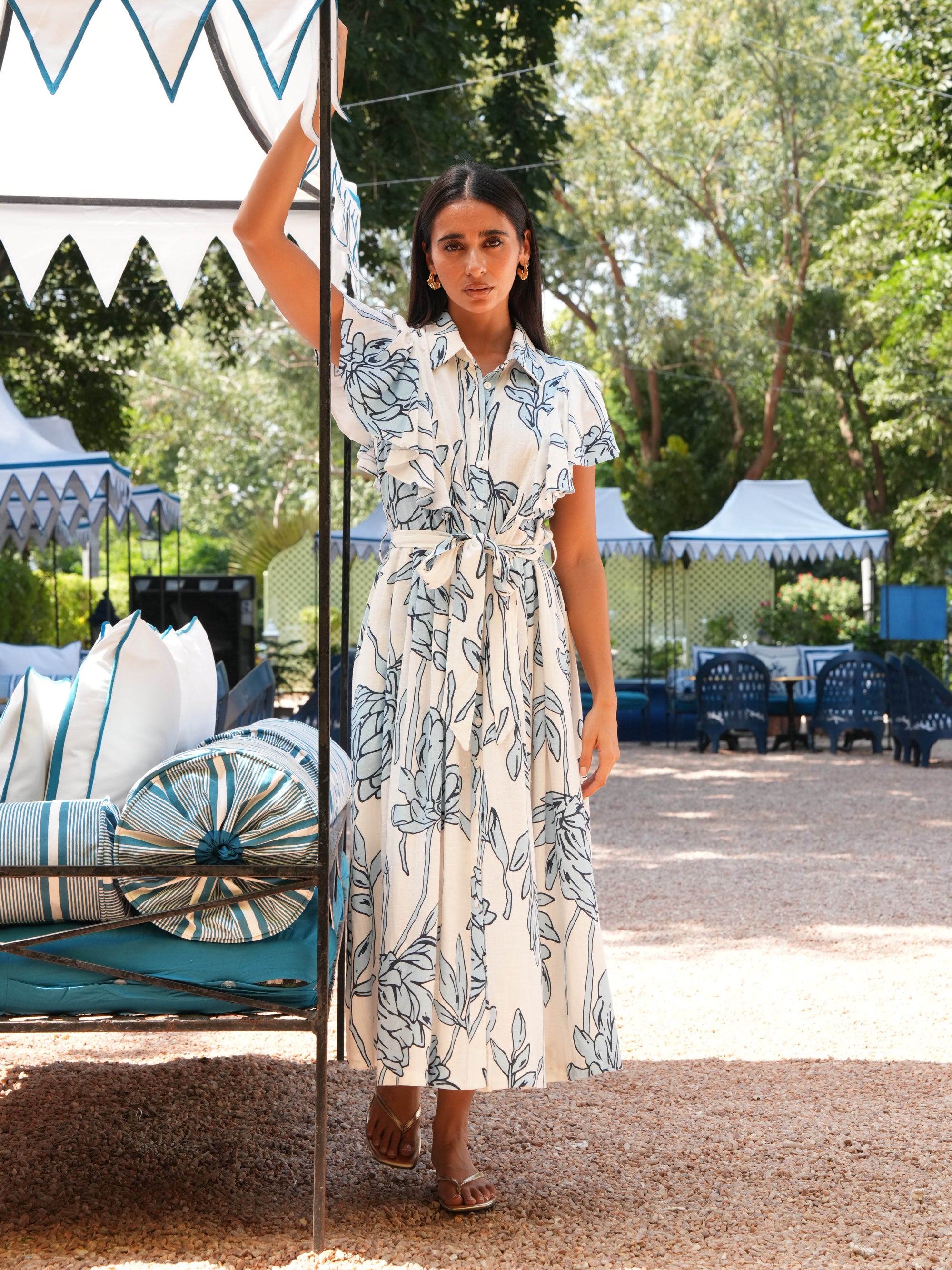 Woman in a floral dress standing outdoors with greenery and outdoor furniture in the background
