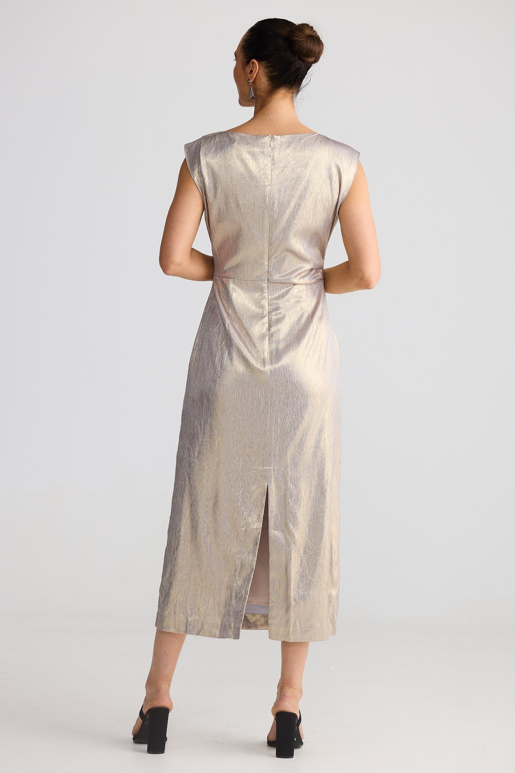 Woman wearing a gold metallic dress with a slit on a white background