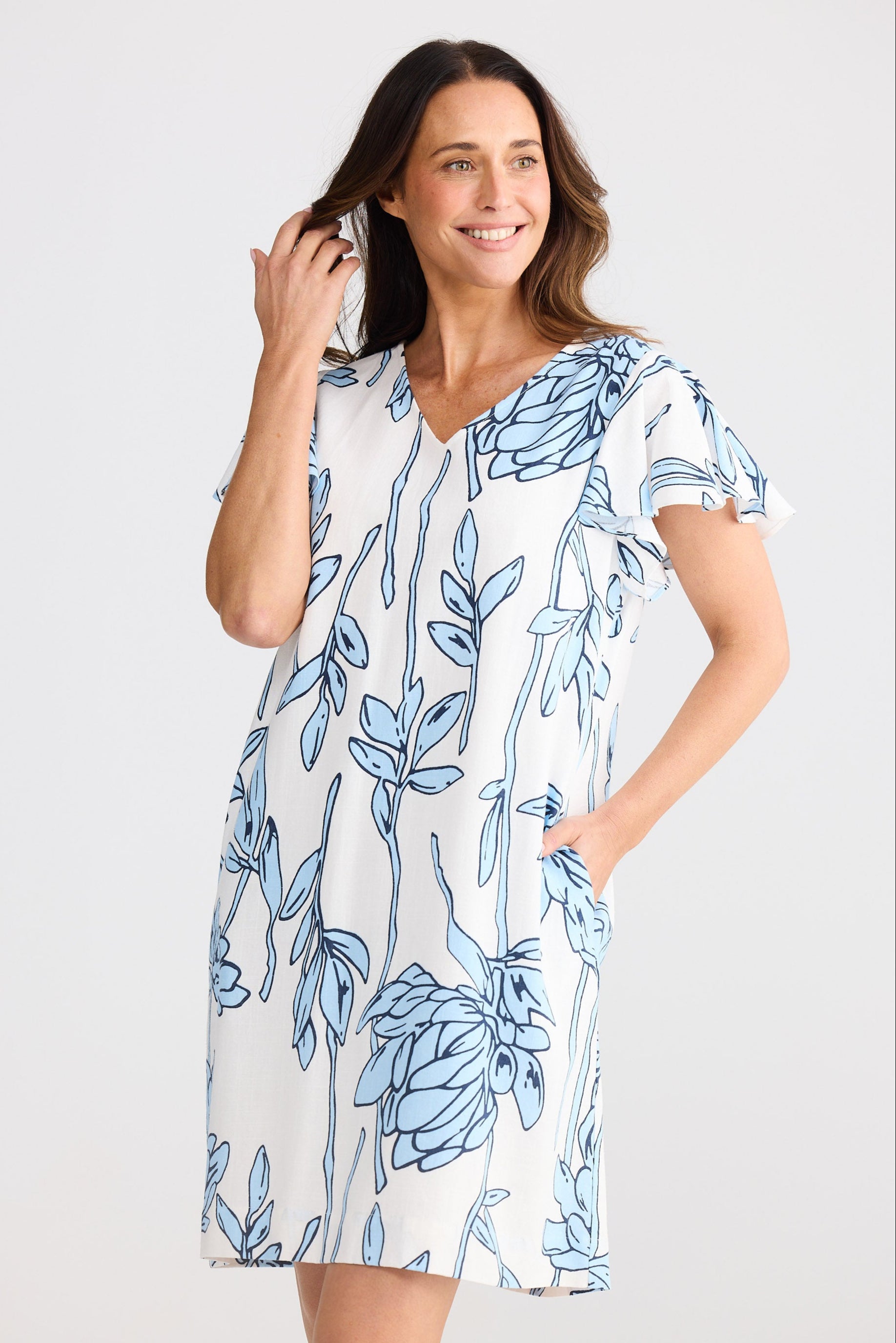 Woman wearing a white dress with blue floral pattern on a plain background