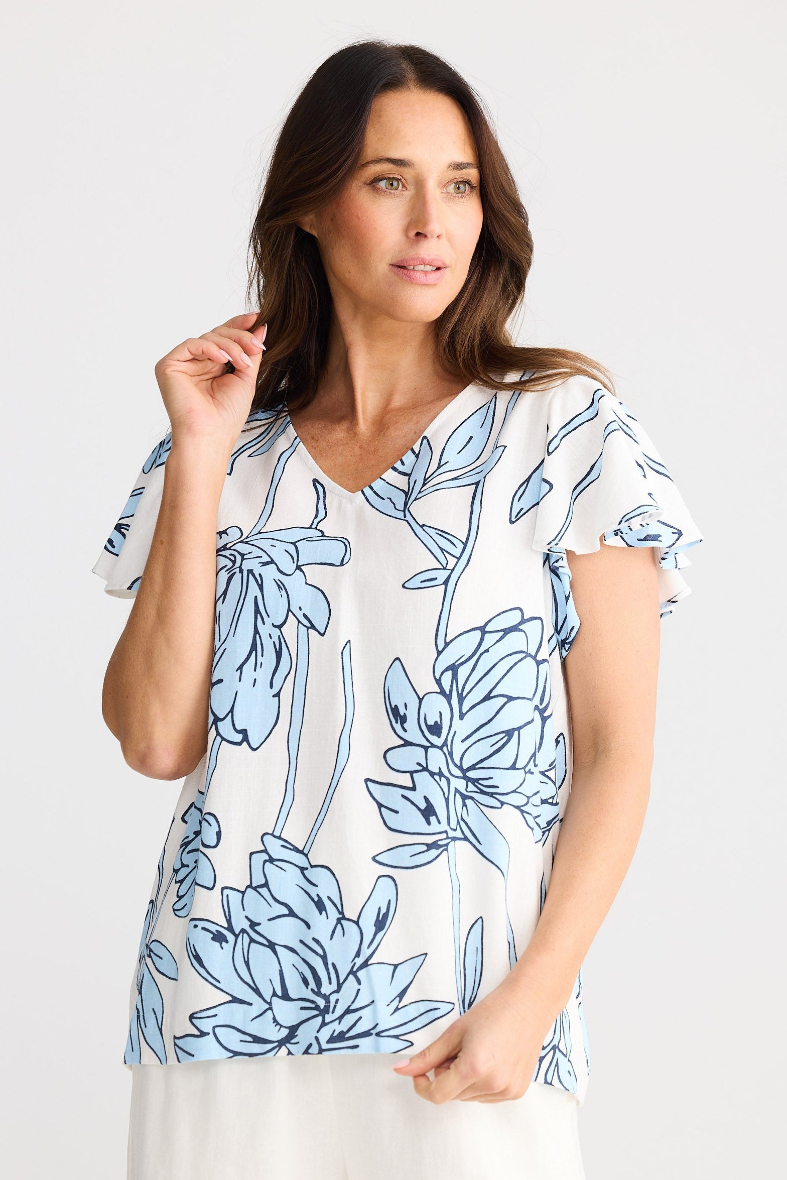 Woman wearing a blue floral top and white pants on a white background