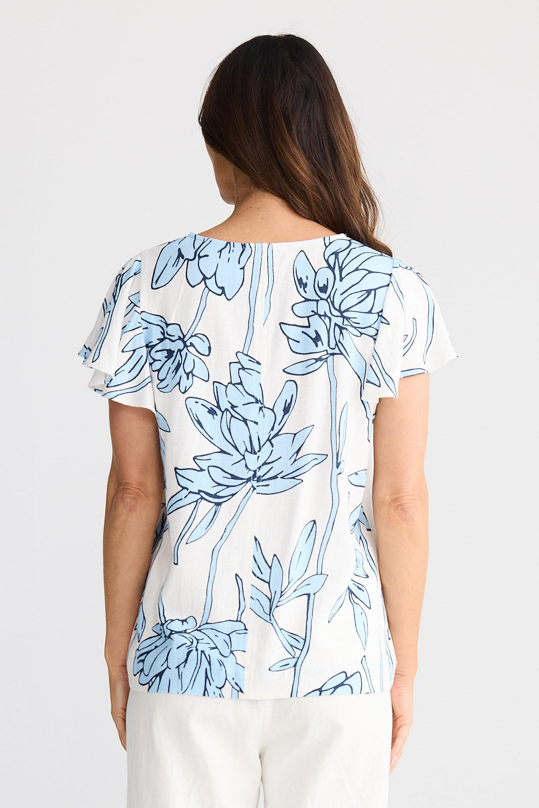 Woman wearing a floral blouse and white pants on a plain background