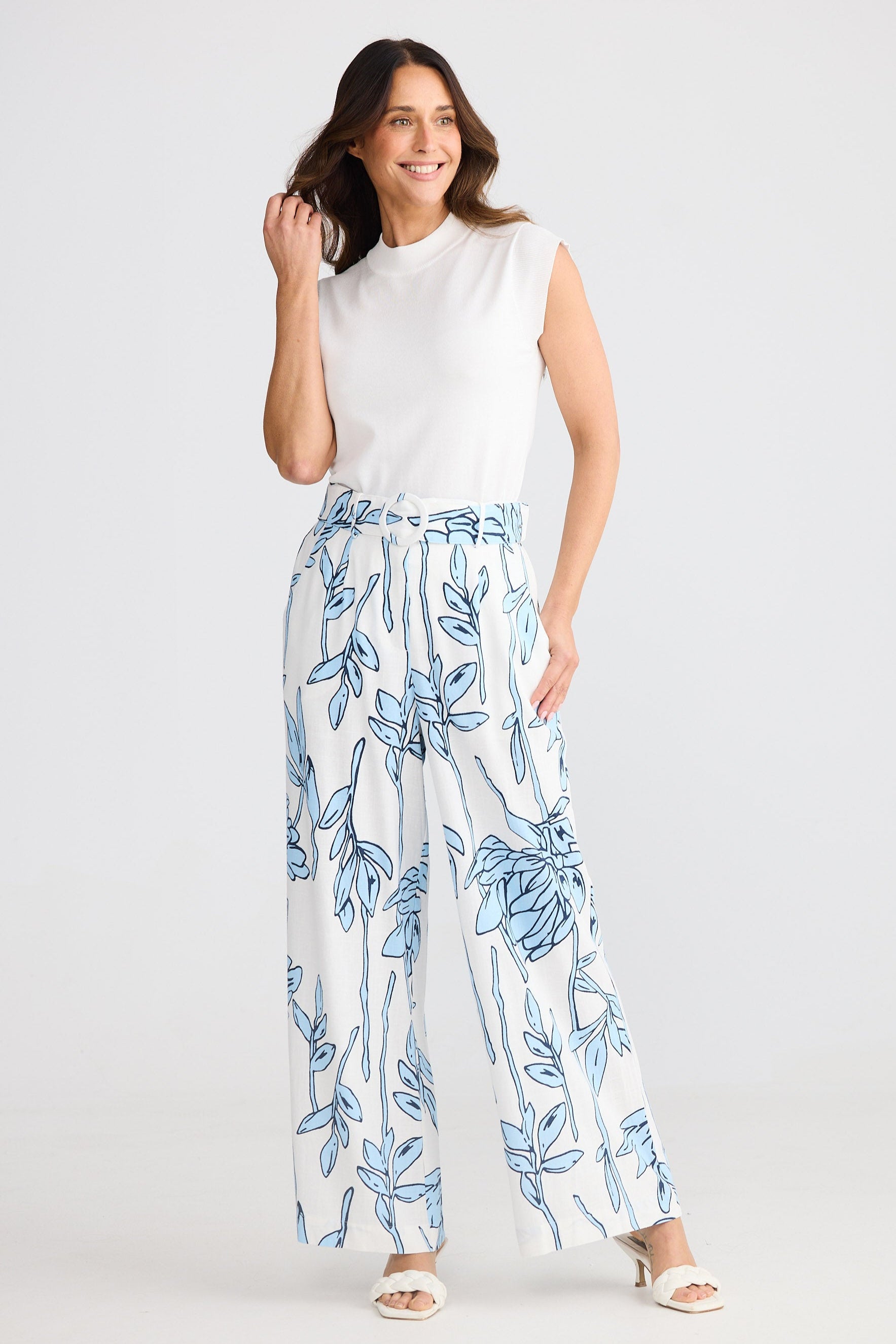 Woman wearing a white sleeveless top and floral pants on a white background
