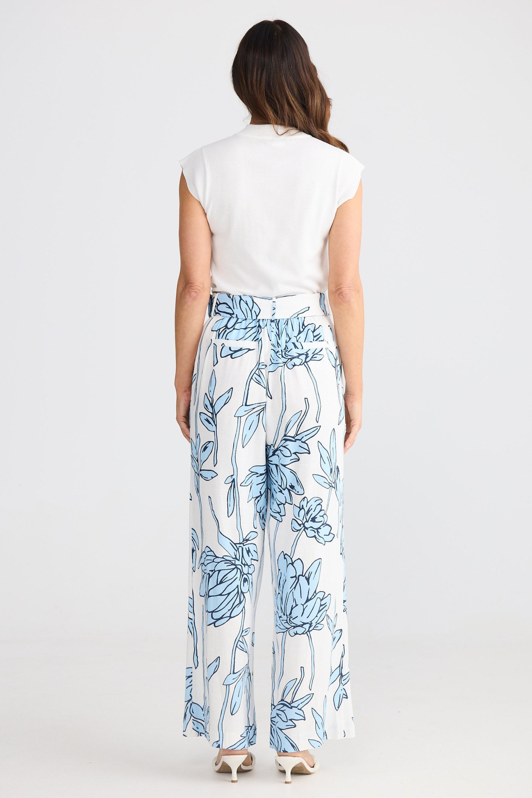 Woman wearing a white top and blue floral pants on a white background