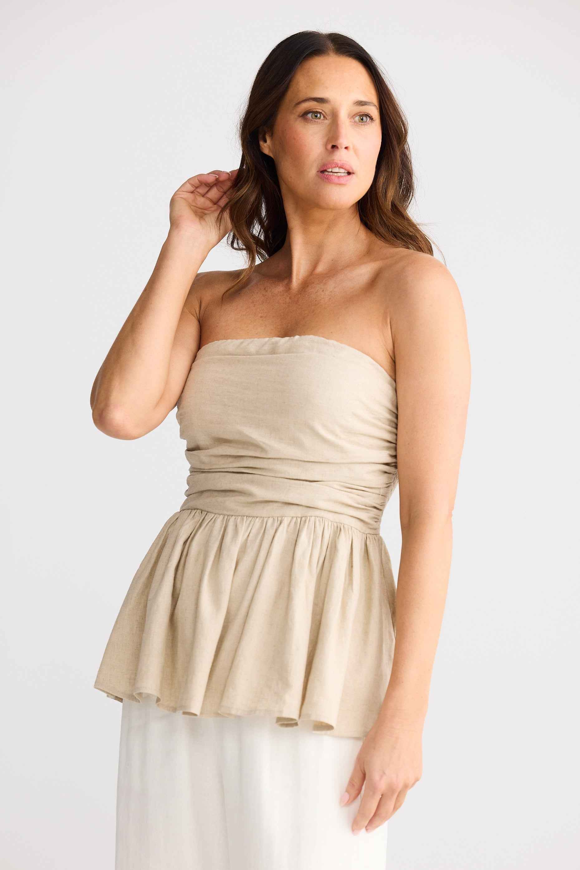 Woman wearing a beige strapless top with a white skirt on a plain background
