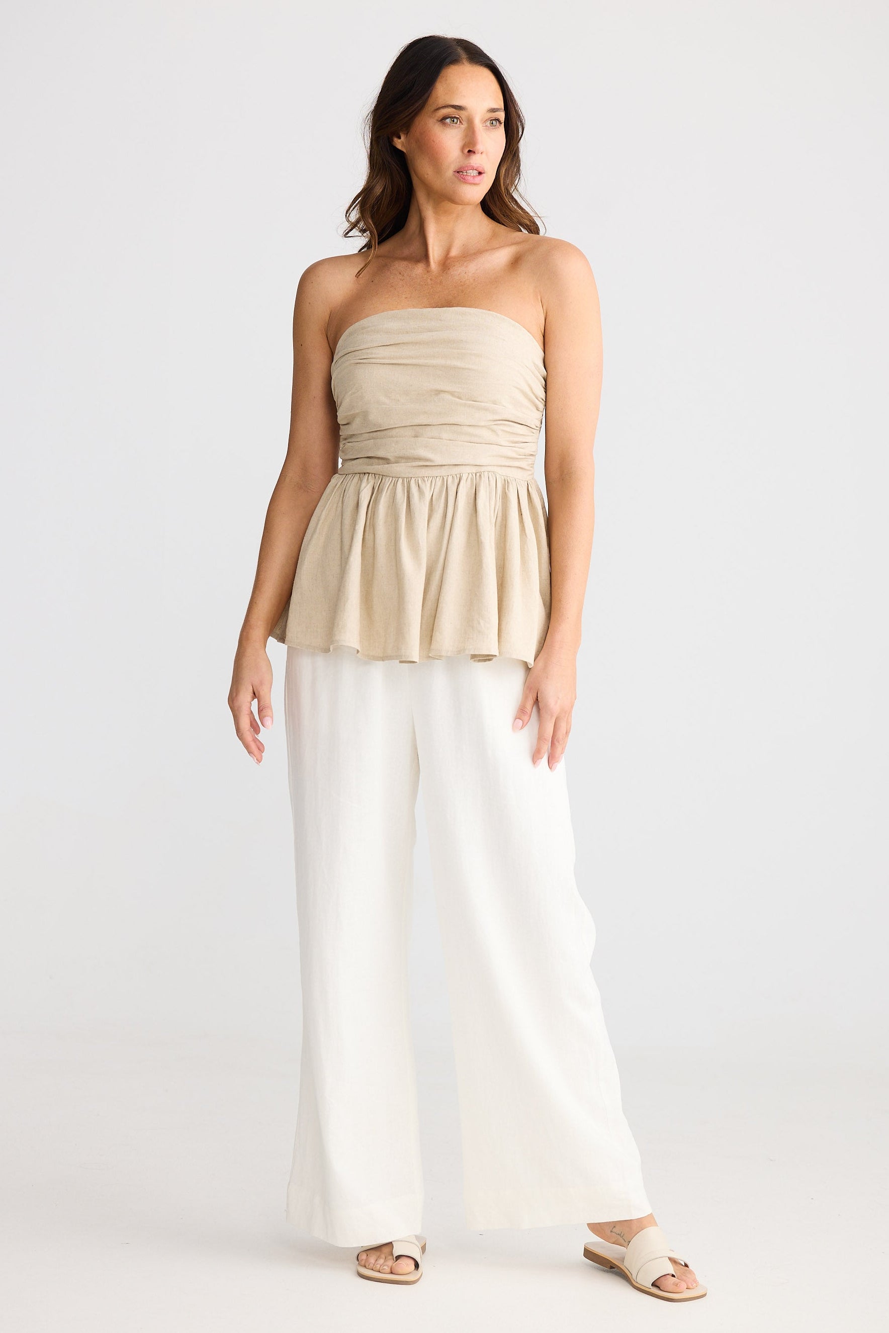 Woman wearing a beige strapless top and white pants on a white background