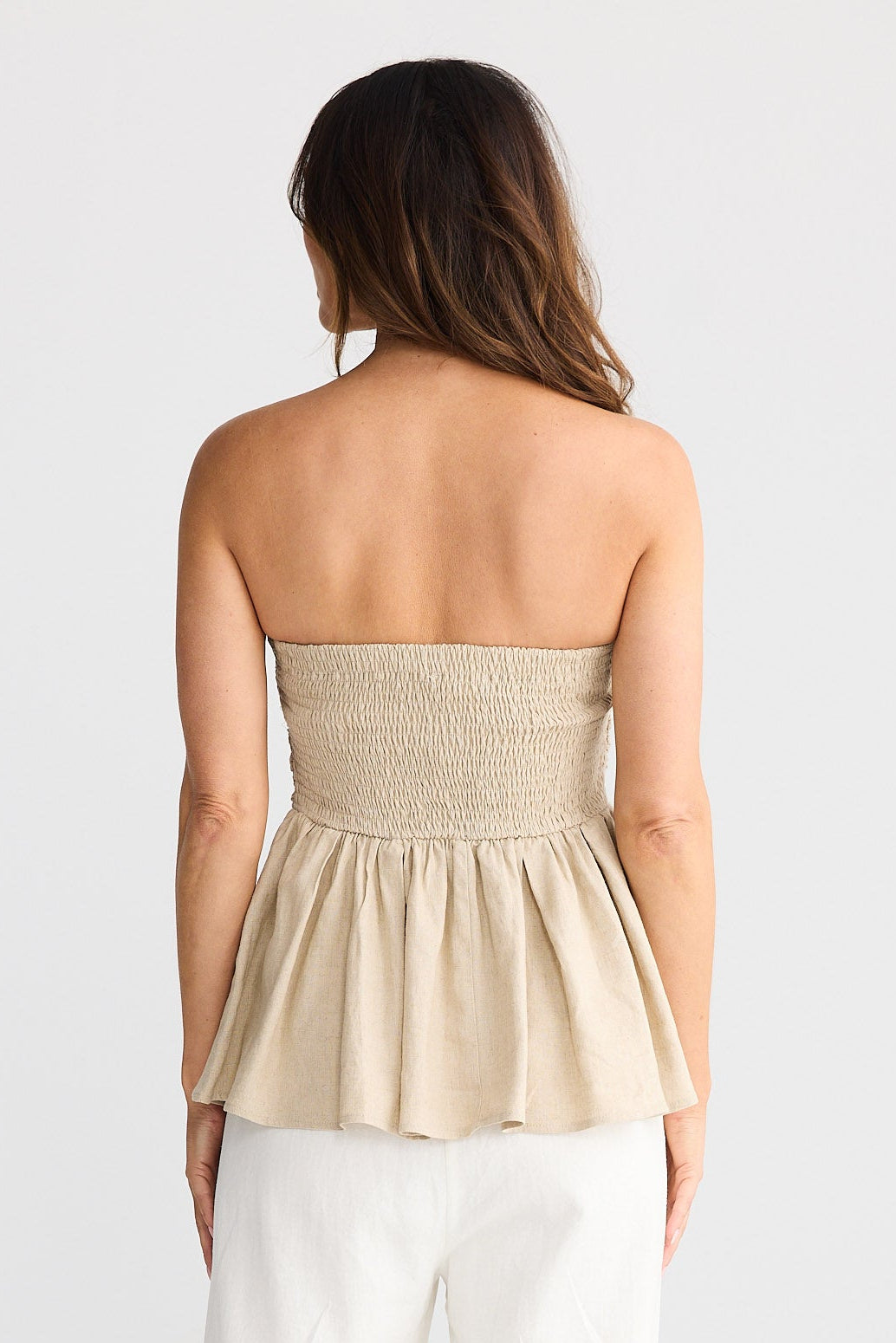 Woman wearing a strapless beige top and white pants on a plain background