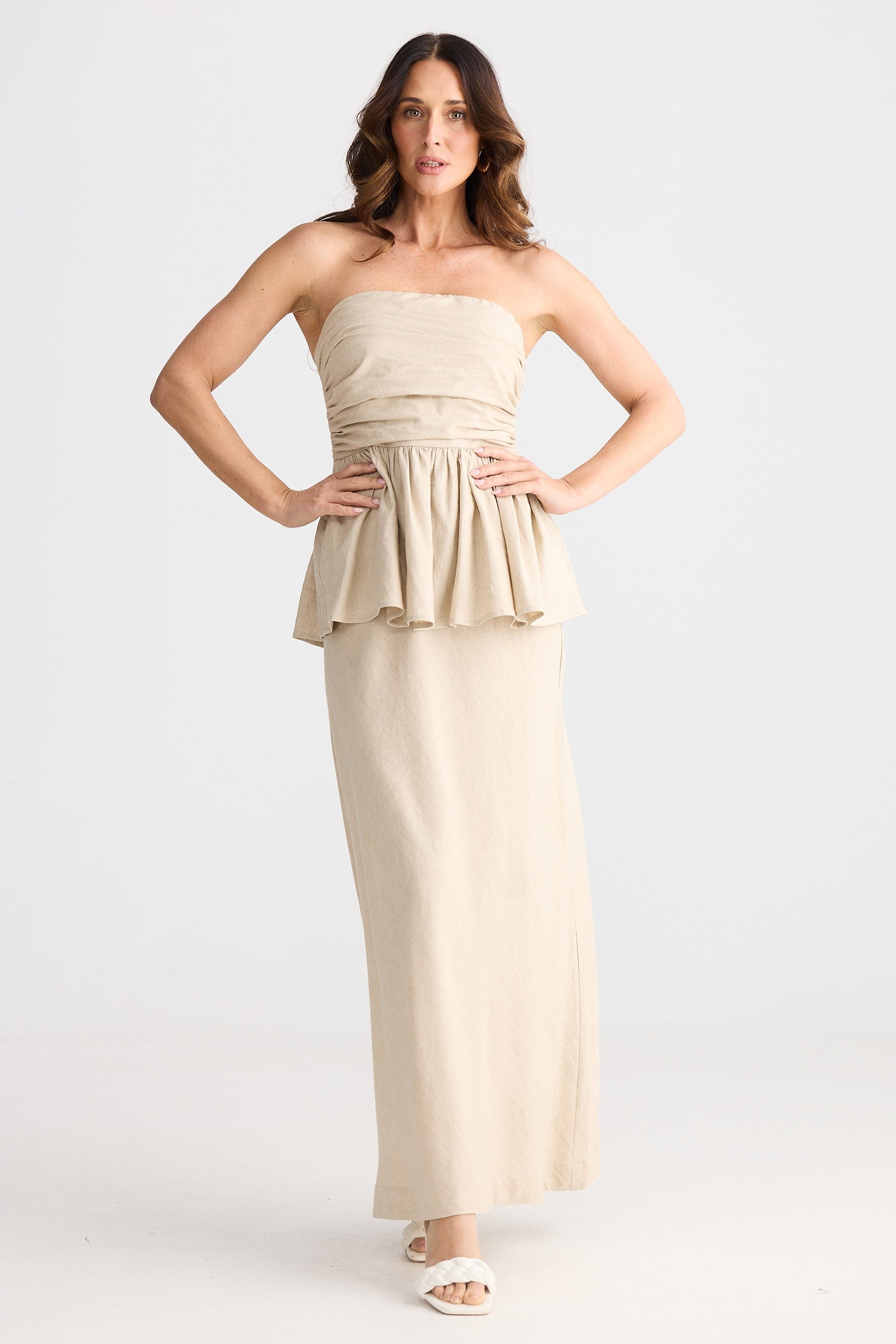 Woman wearing a beige strapless dress with peplum detail on a white background