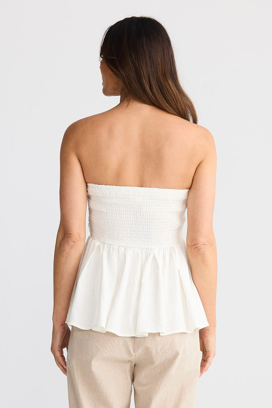 Woman wearing a white strapless top and beige pants on a white background